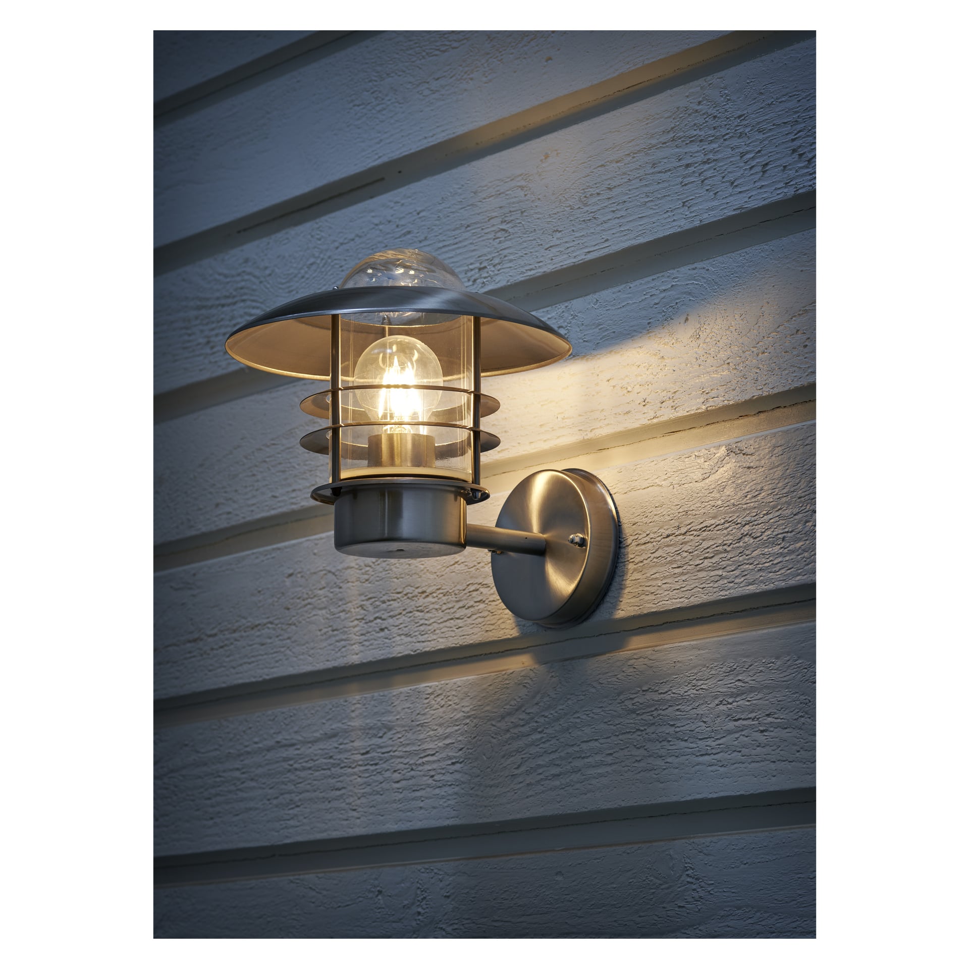 En metallisk EKVAP-vägglampa med synlig glödlampa och cirkulära detaljer är installerad på en ljustonad, horisontellt panelad trävägg som lyser upp omgivningen.