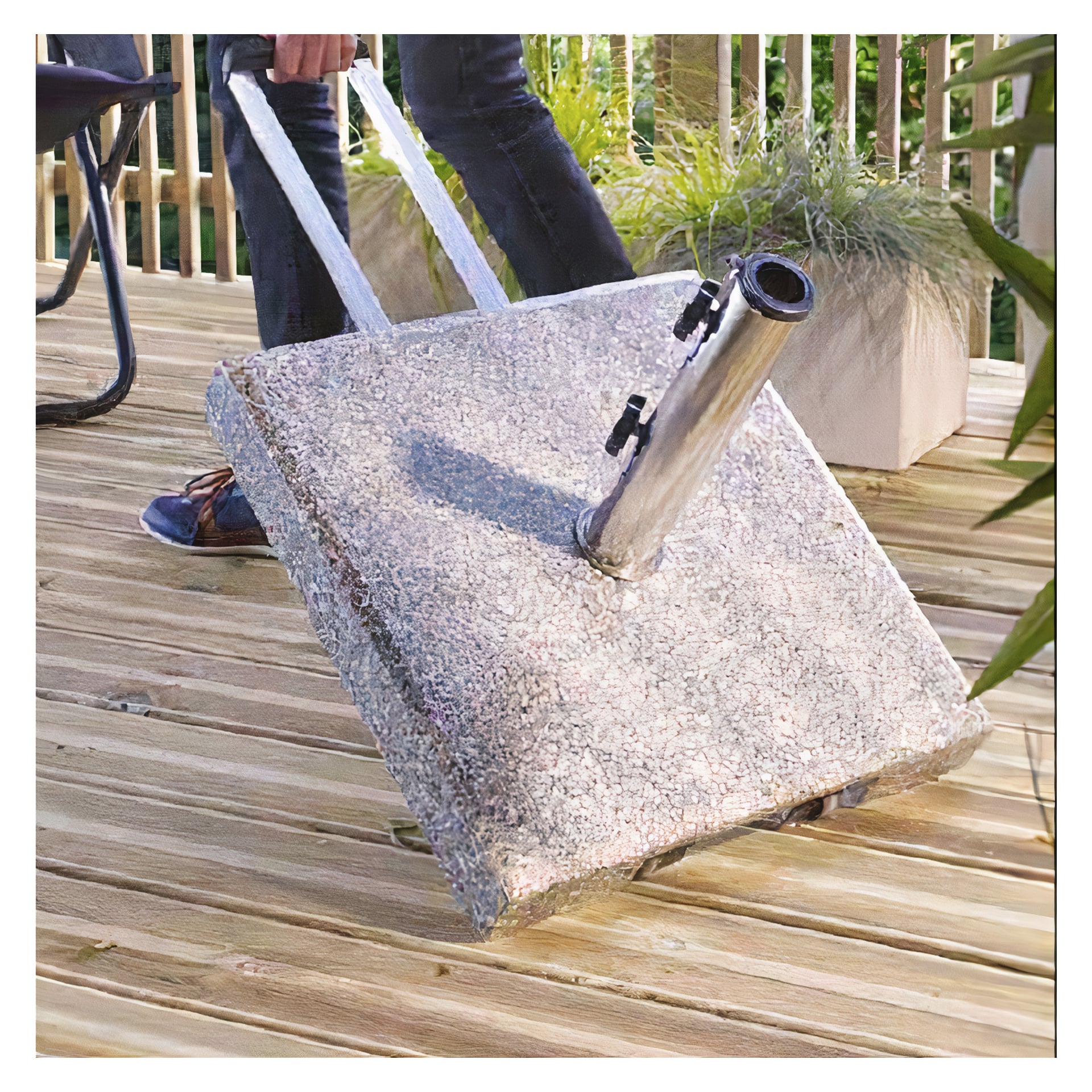 Någon tippar en EKVIP Parasol-bas, som är ett fyrkantigt betongparasollstativ med inbyggda hjul, på en träplatta med krukväxter och utomhussittplatser.