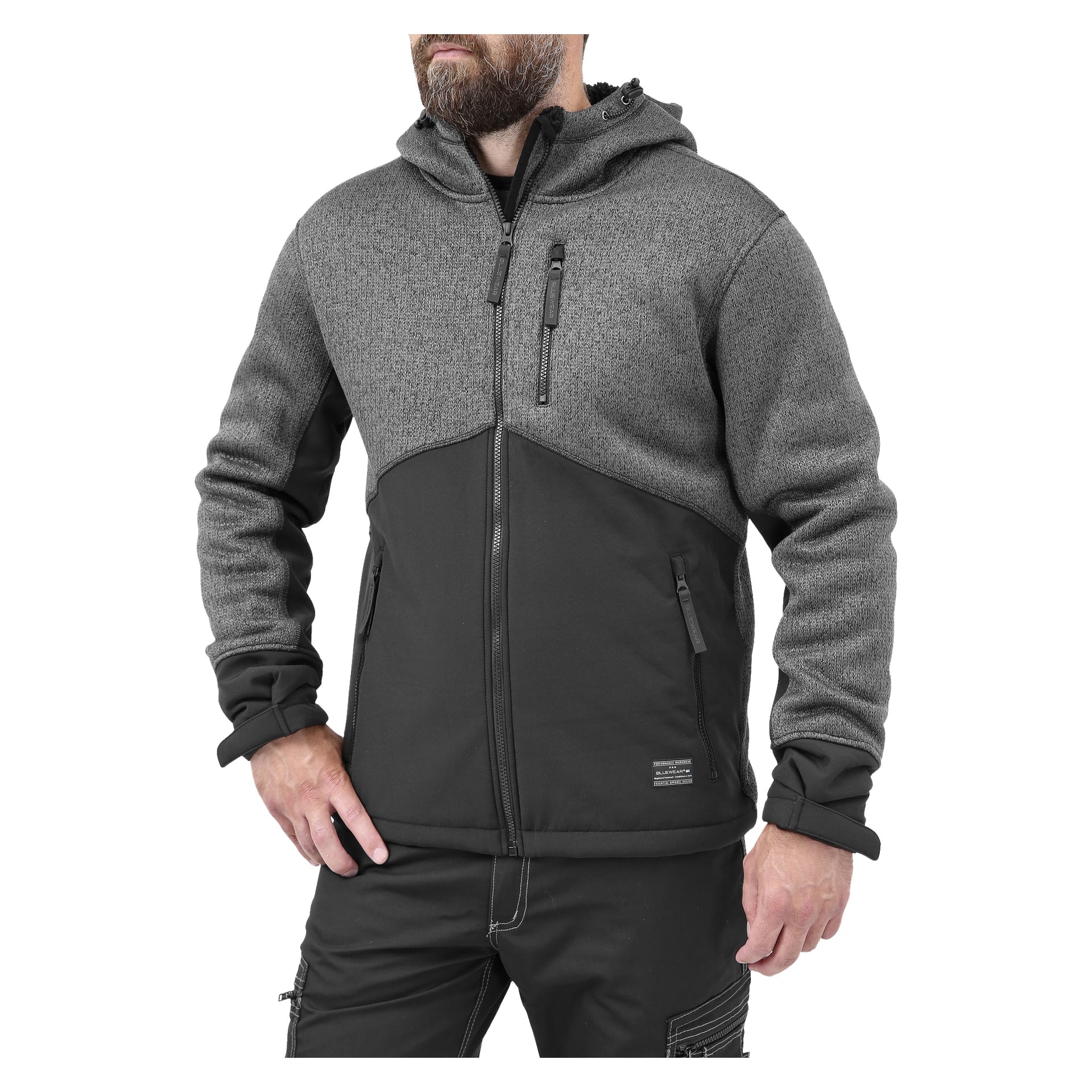 Mies mustissa housuissa mallintaa Bluewear Men's fleece-takkia harmaana ja mustana, korkealla kauluksella ja vetoketjullisilla taskuilla. Toinen käsi on taskussa, toinen roikkuu sivulla.