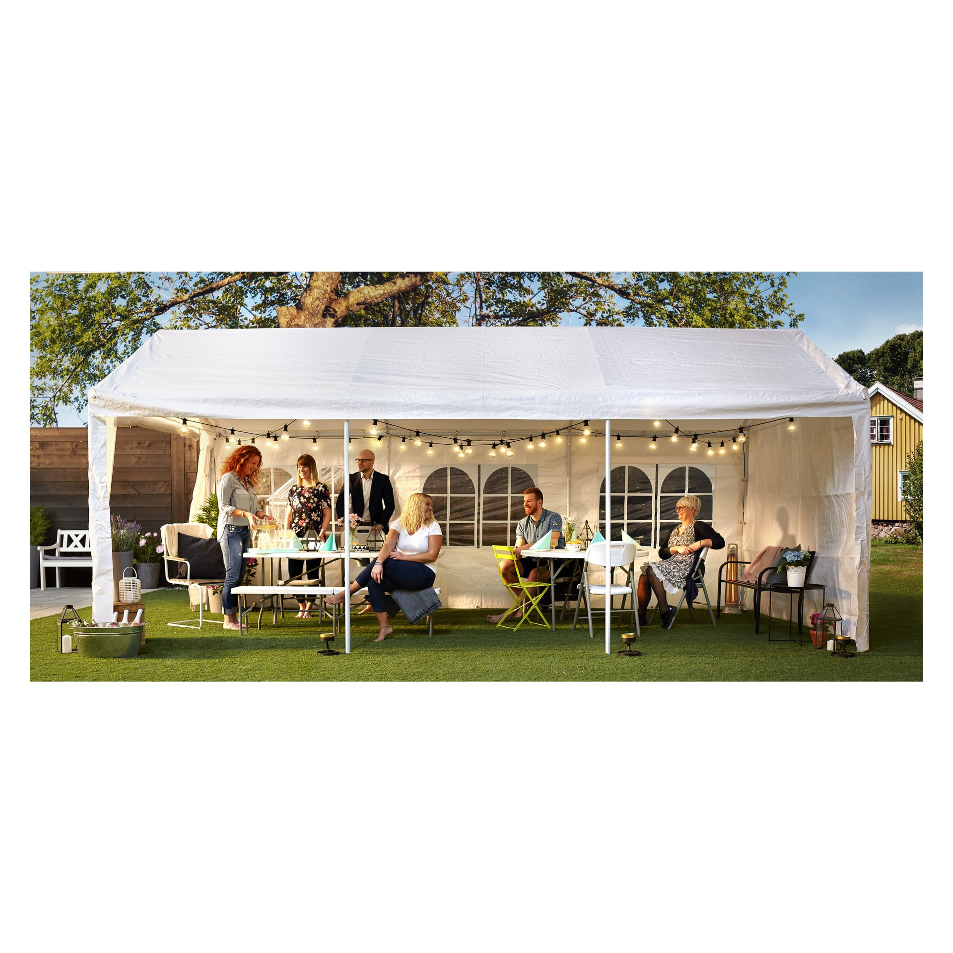 Sju vuxna samlas under ett EKVIP Party-tälttak i en trädgård, sittande och stående runt bord med mat och dryck. Ljusslingor hänger inne i tältet, och ett träd samt ett gult hus syns i bakgrunden.