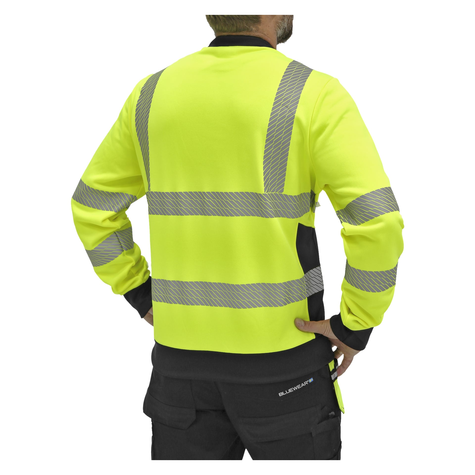 Eine Person steht mit den Händen in die Hüften, gekleidet in einen leuchtend gelben Bluewear-Hi-Vis-Pullover mit reflektierenden grauen Streifen und schwarze Hosen, von hinten betrachtet.
