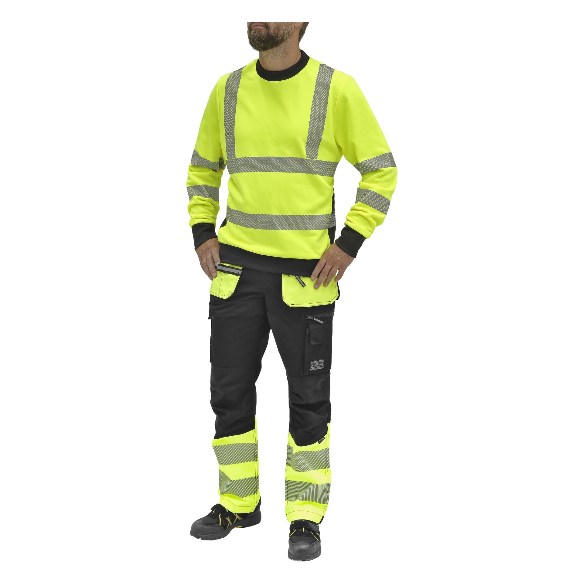 Ein Mann steht mit den Händen in die Hüften gestemmt, gekleidet in einen leuchtend gelben Bluewear Hi-Vis-Pullover mit reflektierenden Streifen. Er trägt schwarze Arbeitshosen mit gelben und grauen reflektierenden Details sowie schwarze Sicherheitsschuhe.
