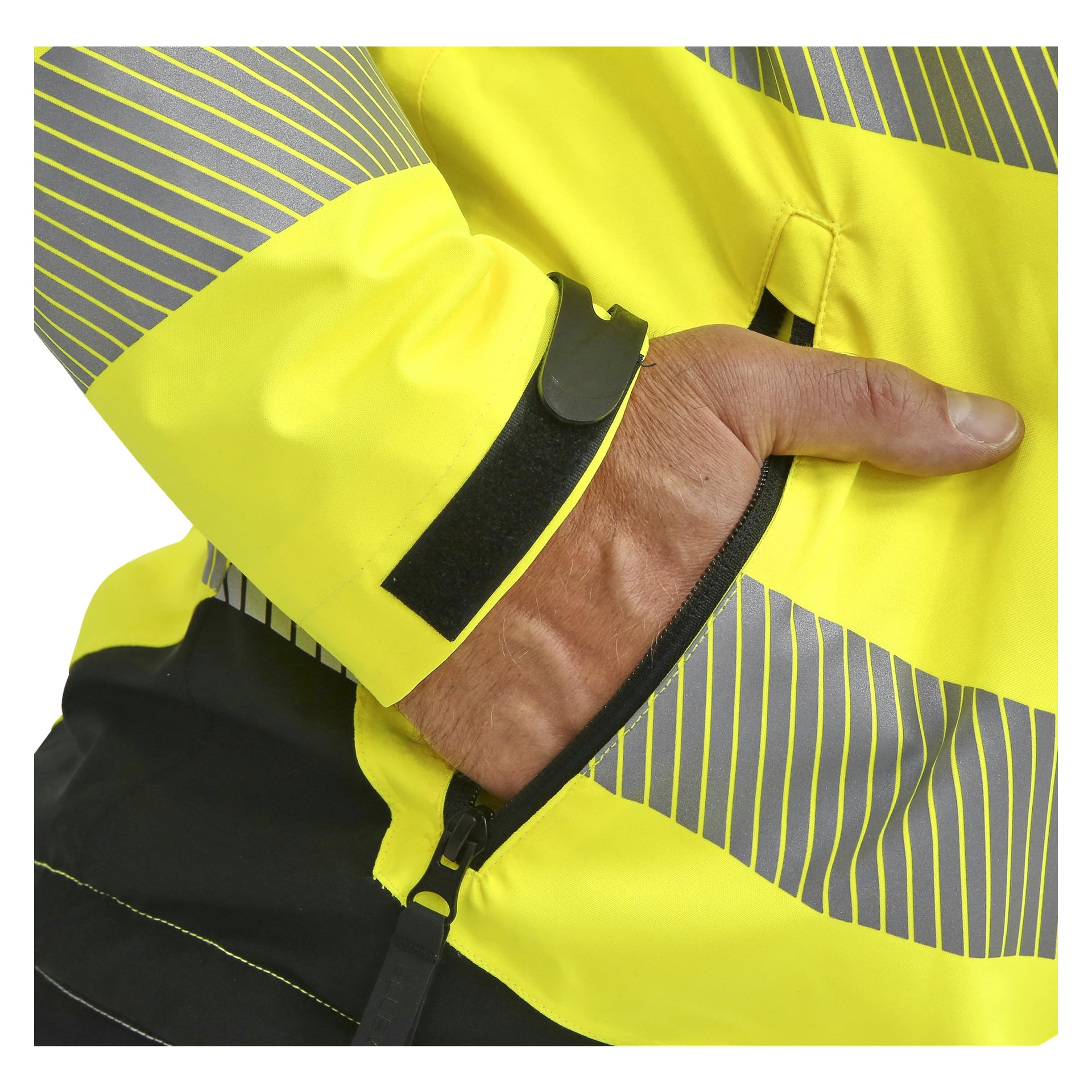 En person visas i en Bluewear Hi-Vis-jacka med gula och grå ränder, svart dragkedja och vänster hand nedstoppad i en ficka med dragkedja. Jackans ärm har en svart hak- och ögla-fästrem.