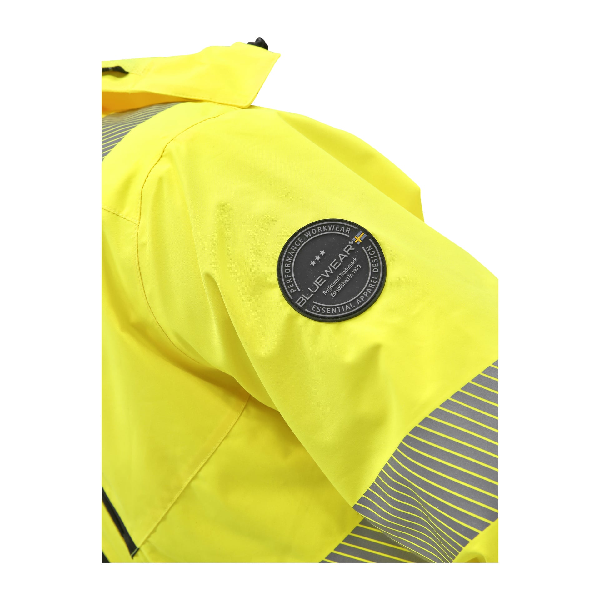 En närbild av en Bluewear Hi-Vis-jackärm, som visar en rund svart och grå lapp med orden BLÅKLÄDER ESSENTIAL APPAREL, och reflekterande grå ränder på ärmmanchetterna.