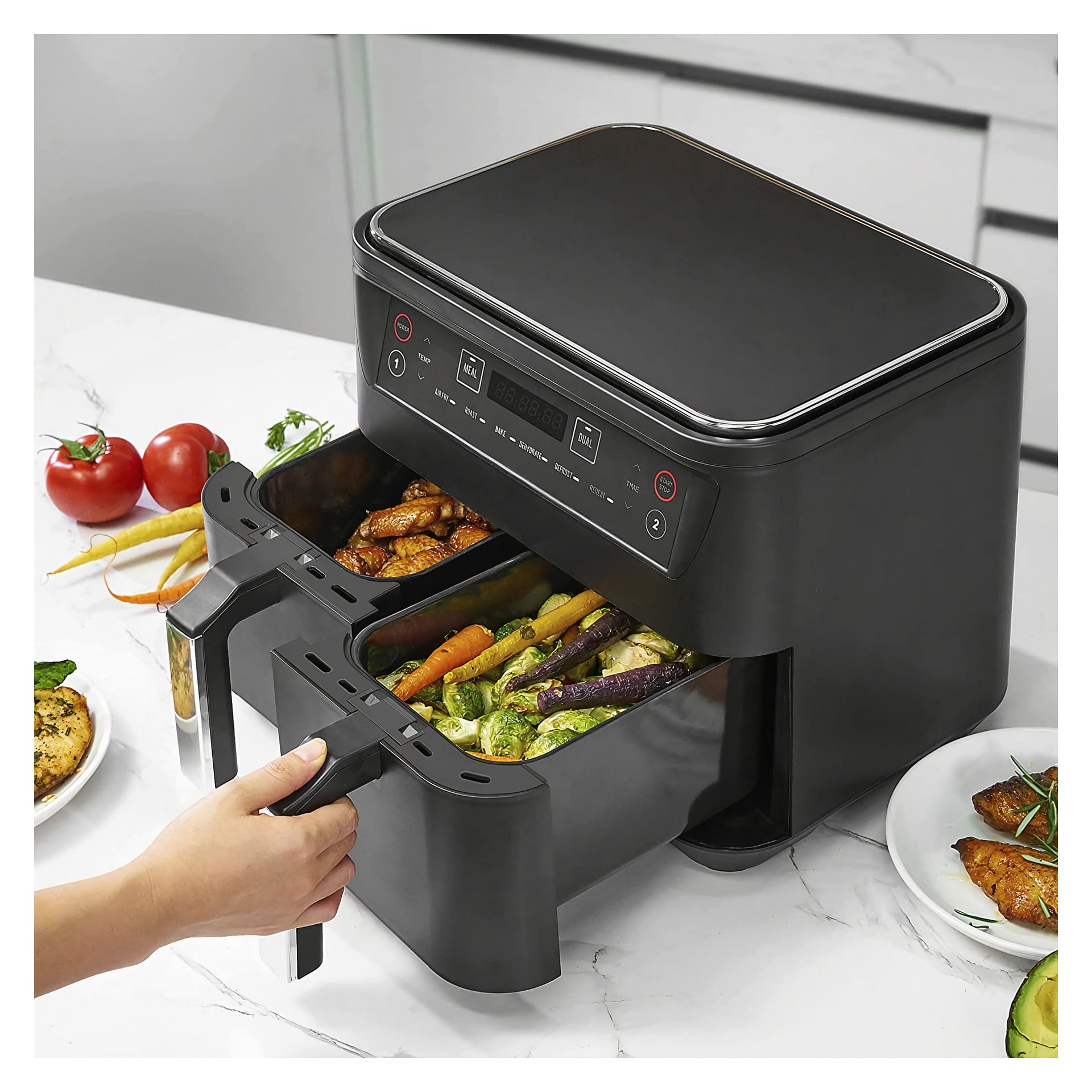 En hand öppnar en svart Bright Hot Air Deep-Fryer med två korgar på köksbänken. Korgarna fylls med rostade grönsaker och kyckling, och tallrikar med mat tillsammans med färska tomater är placerade runt fritösen.