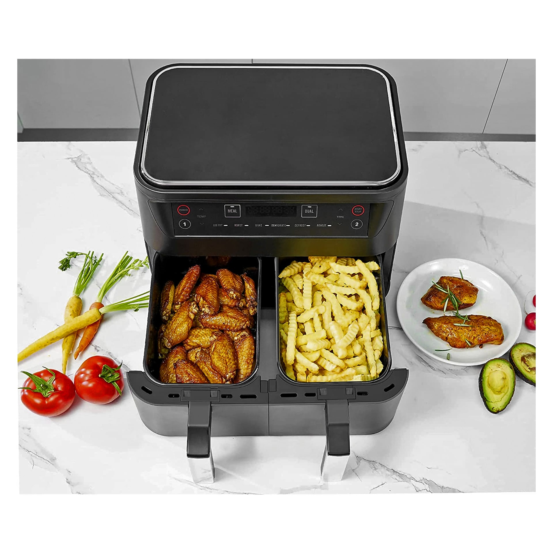 En ljus varmluftsfritös med två korgar står på köksbänken, fylld med krispiga kycklingvingar och gyllene pommes frites. Runt omkring finns färska grönsaker, avokadoskivor och en tallrik med grillad kycklingbröst och körsbärstomater.