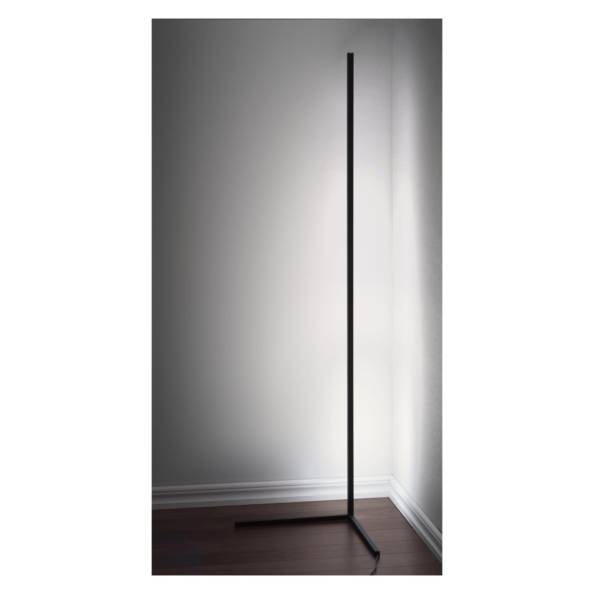 En smal, minimalistisk svart EKVIP Floor Lamp LED är placerad i ett rumshörn med vita väggar och mörka trägolv. Sladden sträcker sig längs golvet vid golvlisterna.