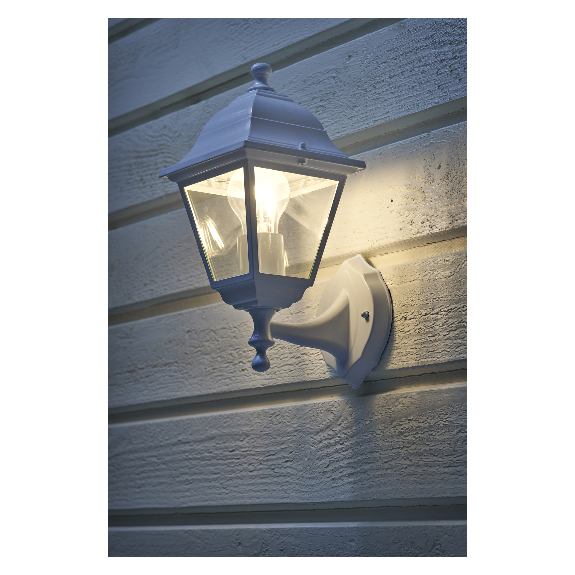 En EKVAP vägglampa med vit armatur är fäst på horisontell träpanel. Dess ljus lyser upp området runtomkring, skapar skuggor och framhäver träets textur.