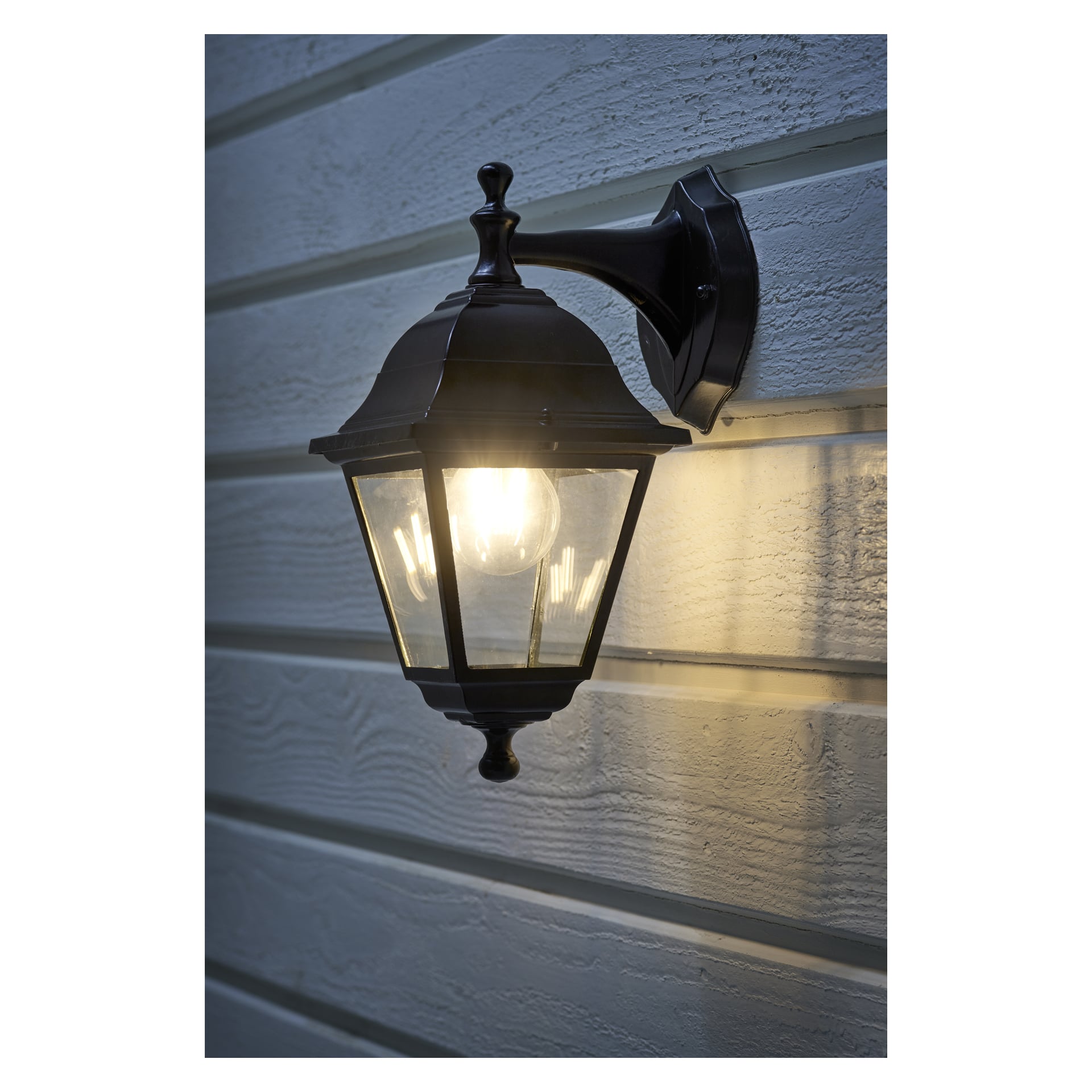 En svart EKVAP-vägglampa med ett klart glashus är installerad på en ljus trävägg och avger ett milt, varmt sken som sprider sig över träpanelerna.