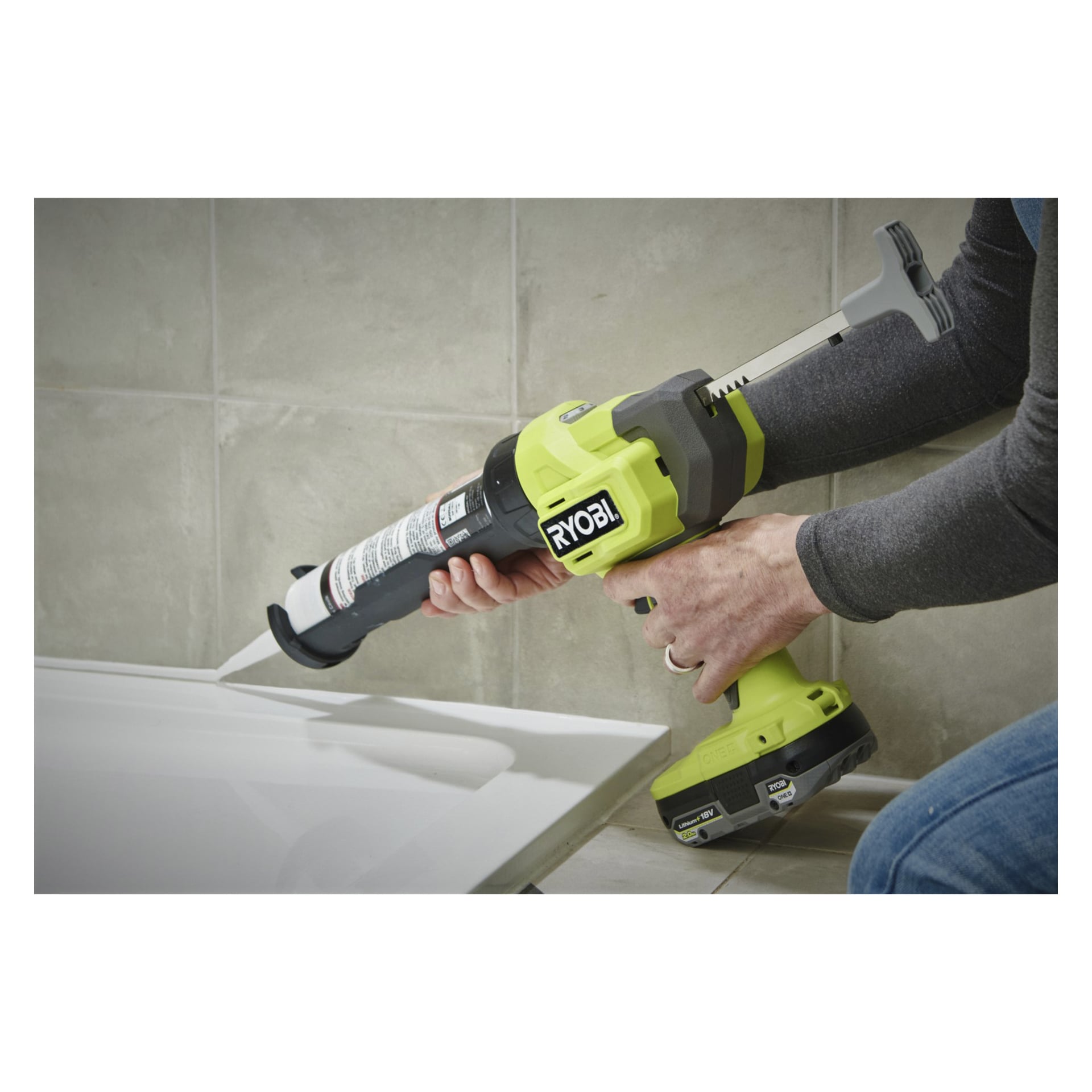 Någon applicerar fogmassa med en Ryobi One+ Battery-driven fogpistol RCG18‐0 längs kanten av en vit yta, grå kaklade väggar synliga bakom.