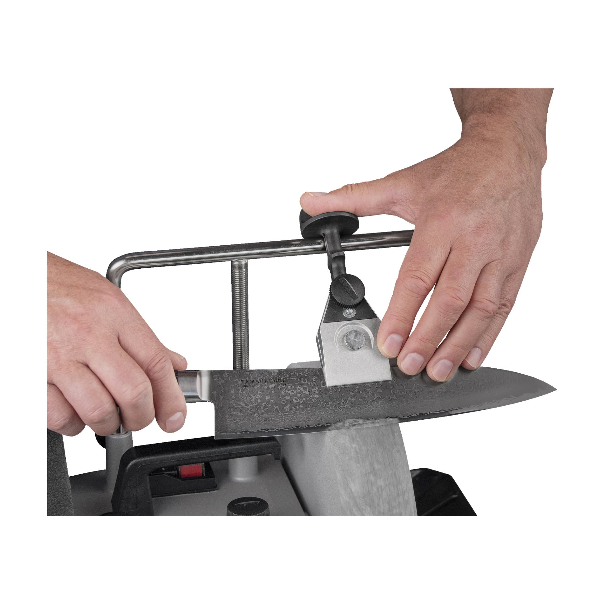 Någon använder Tormek Grinding Jig KJ-45, fäst vid en slipmaskin, för att slipa en stor kökskniv och håller den försiktigt på plats när dess egg nuddar spinnhjulet.