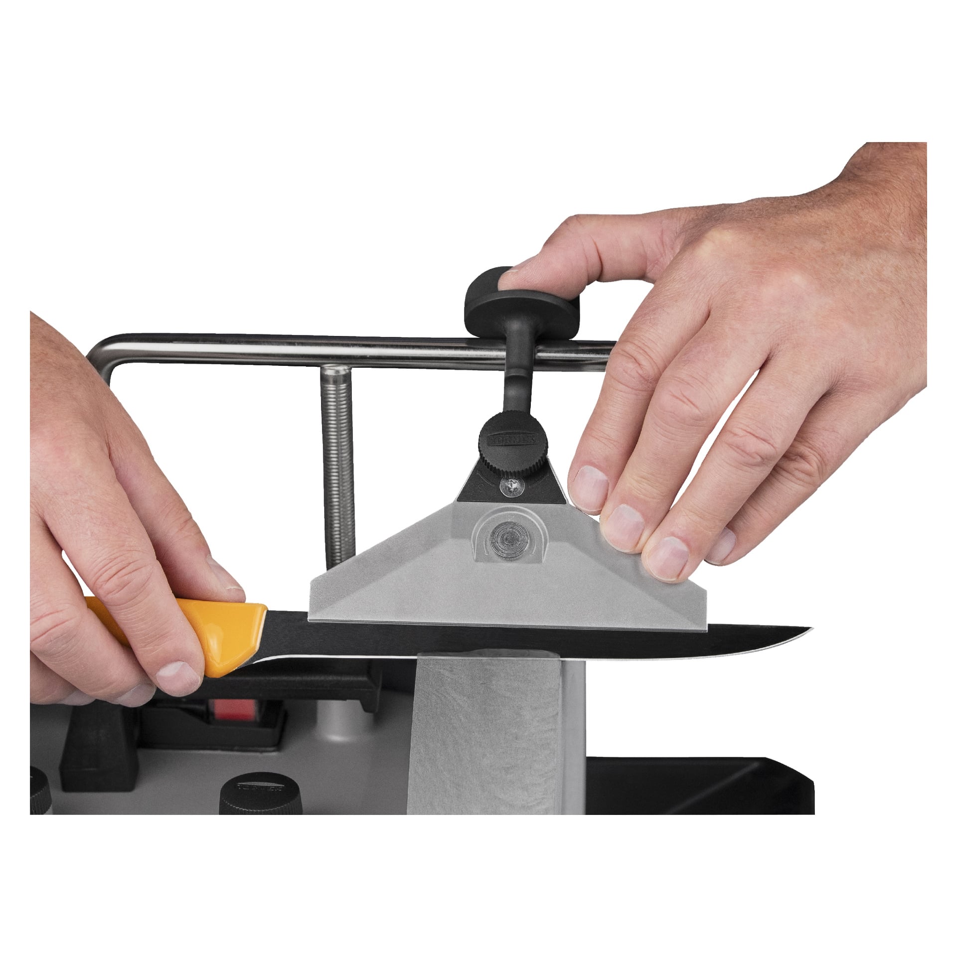 Man använder Tormek Grinding jigg KJ-140 för att slipa en kniv, greppar jiggens handtag med ena handen och stabiliserar bladet med den andra för att hålla en jämn vinkel mot slipstenen.