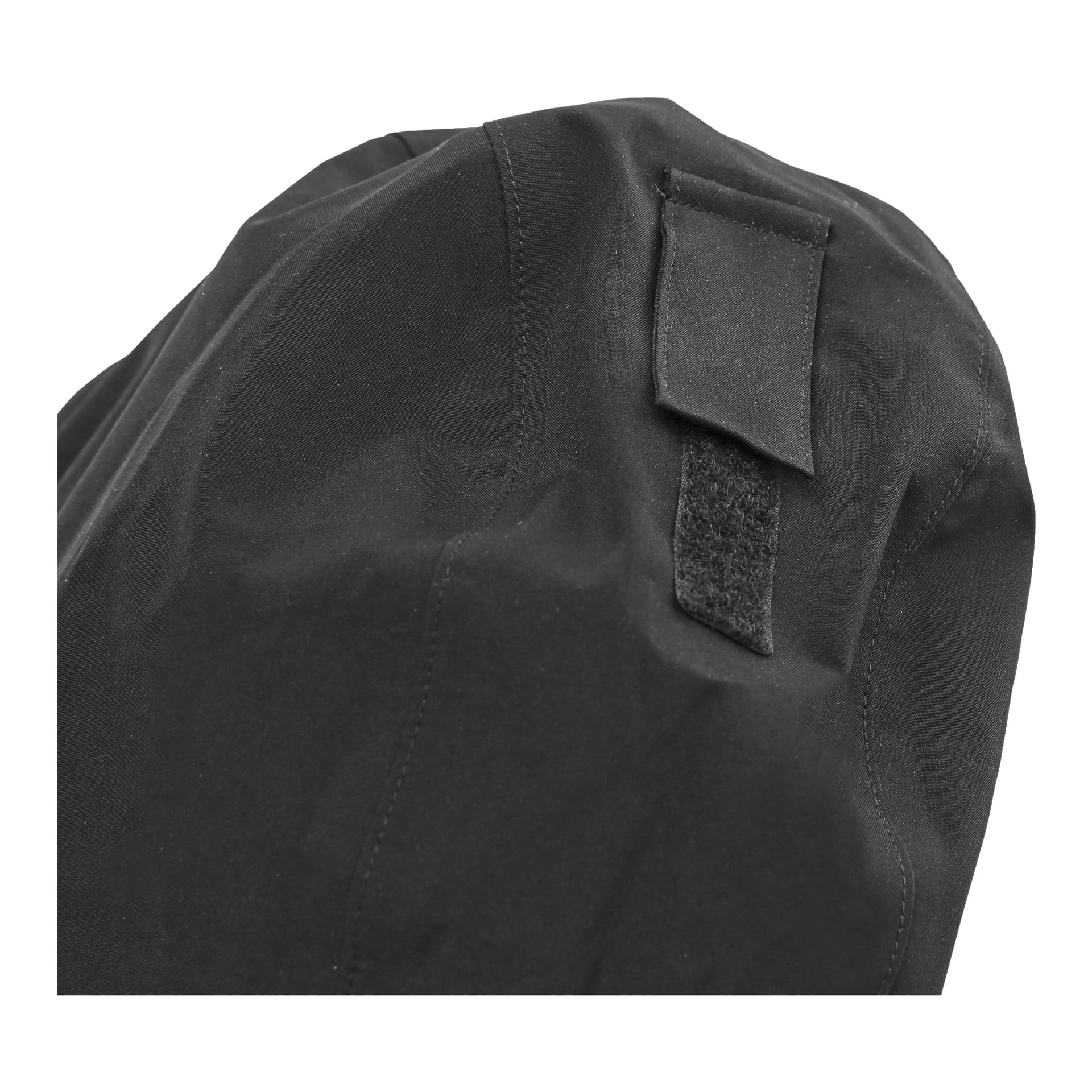 En detaljerad vy av Kayoba Outdoor damshelljacka visar svart tyg med en rektangulär kardborrelapp och en flik. Bilden fångar materialets synliga sömmar och texturer, även om det är oklart vilken funktion dessa specifika funktioner fyller.
