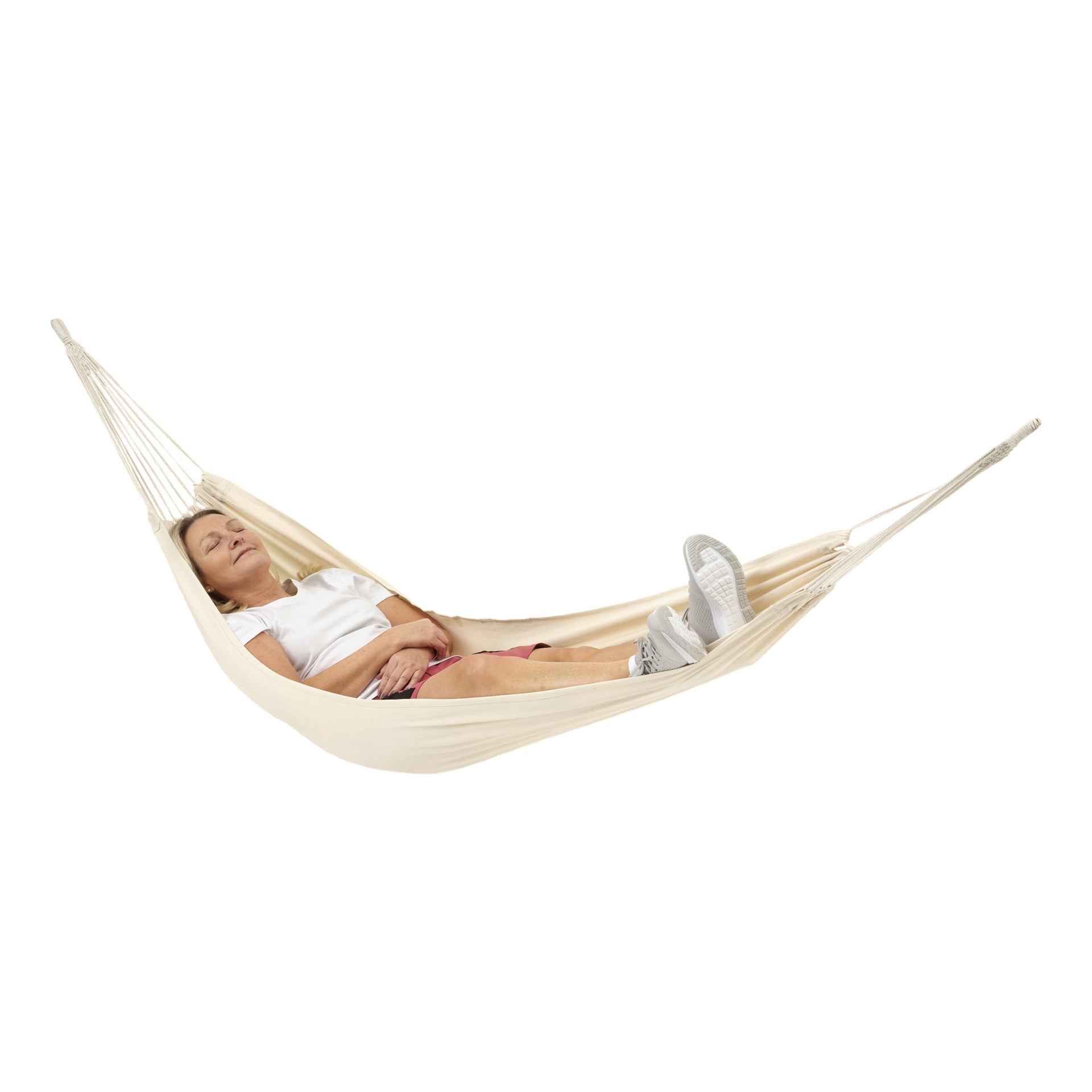 En person slappnar av i en krämfärgad Kayoba-hängmatta, med slutna ögon, armar i kors och benen utsträckta. De är klädda i en vit skjorta och rosa shorts.