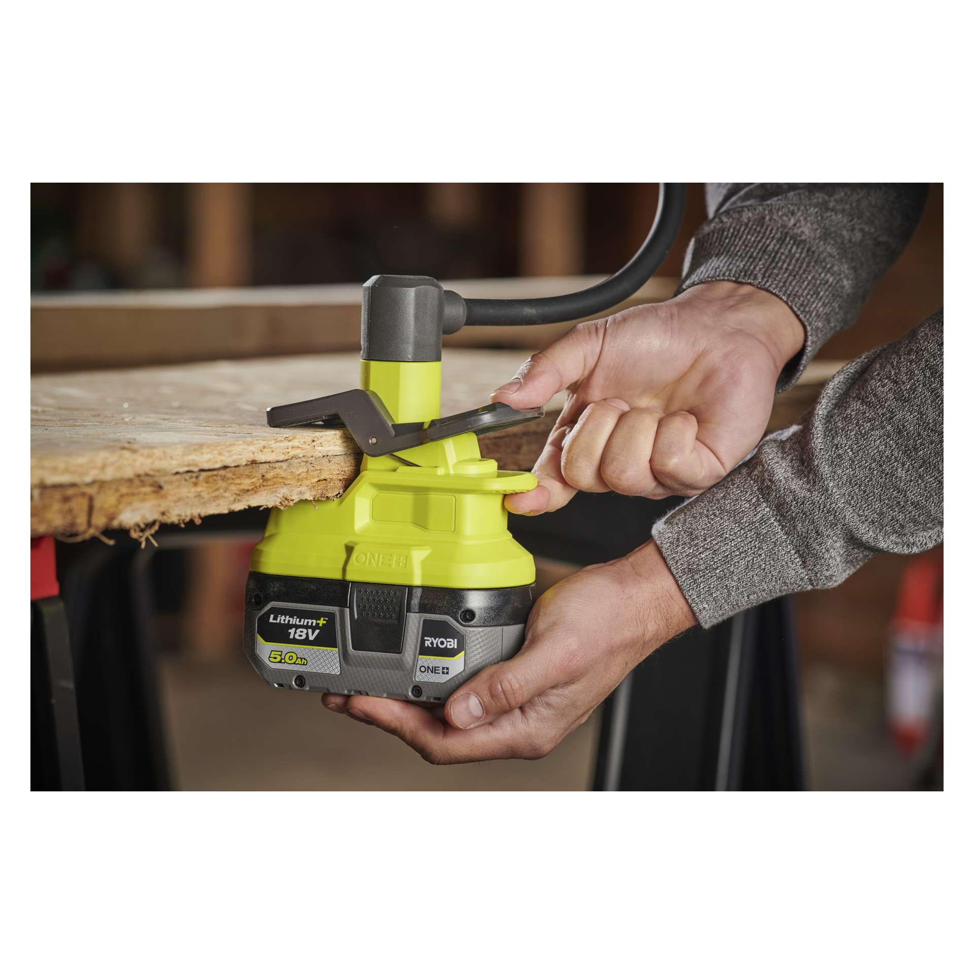 Man jobber med begge hender på en arbeidsbenk, og bruker Ryobi One+ batteridrevne LED-arbeidslampe med klemme RLCF18-0 for å lyse opp grovt treverk.