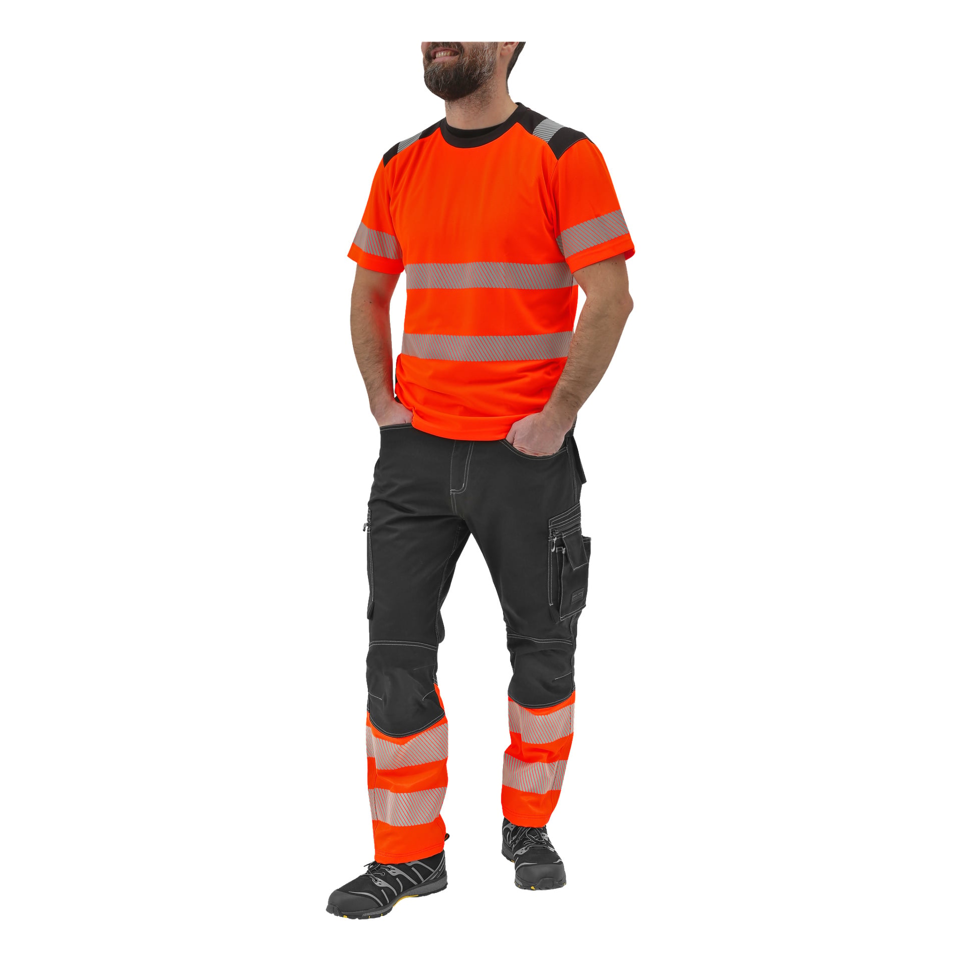 En person står med händerna i fickorna, klädd i en klarorange Bluewear kortärmad hög-vis-skjorta med reflekterande ränder, tillsammans med svarta cargobyxor och svarta arbetsskor, båda också accentuerade med reflekterande ränder.