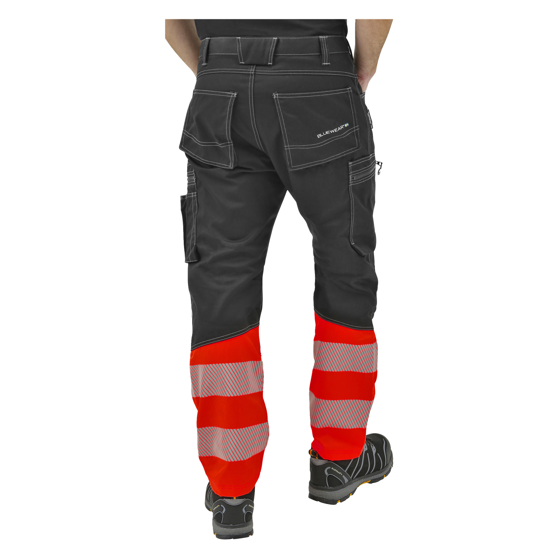 Die Person trägt eine schwarze Arbeitshose mit weißen Nähten, orangefarbenen reflektierenden Streifen an den Unterschenkeln und schwarzen Arbeitsschuhen. Die Hose hat mehrere Taschen und ein "Bluewear"-Etikett auf der Gesäßtasche. Die Person steht mit dem Gesicht zur Seite.