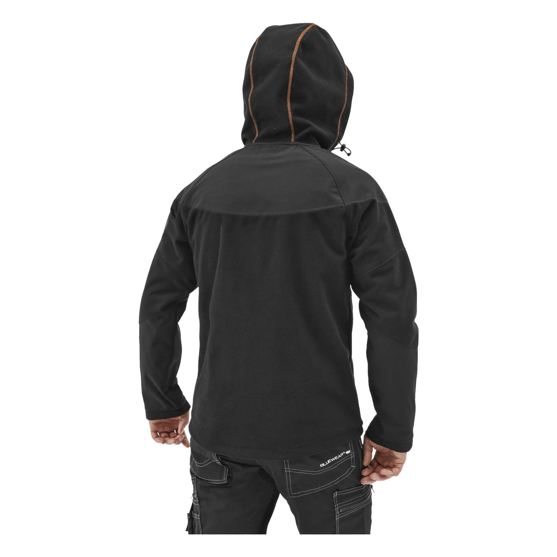 En person står med ryggen mot ryggen, klädd i en svart Bluewear Pro Workwear Men's vindtät fleecejacka med orange sömmar. Deras händer är avslappnade vid sidorna, och de bär också svarta byxor med synliga stygn.