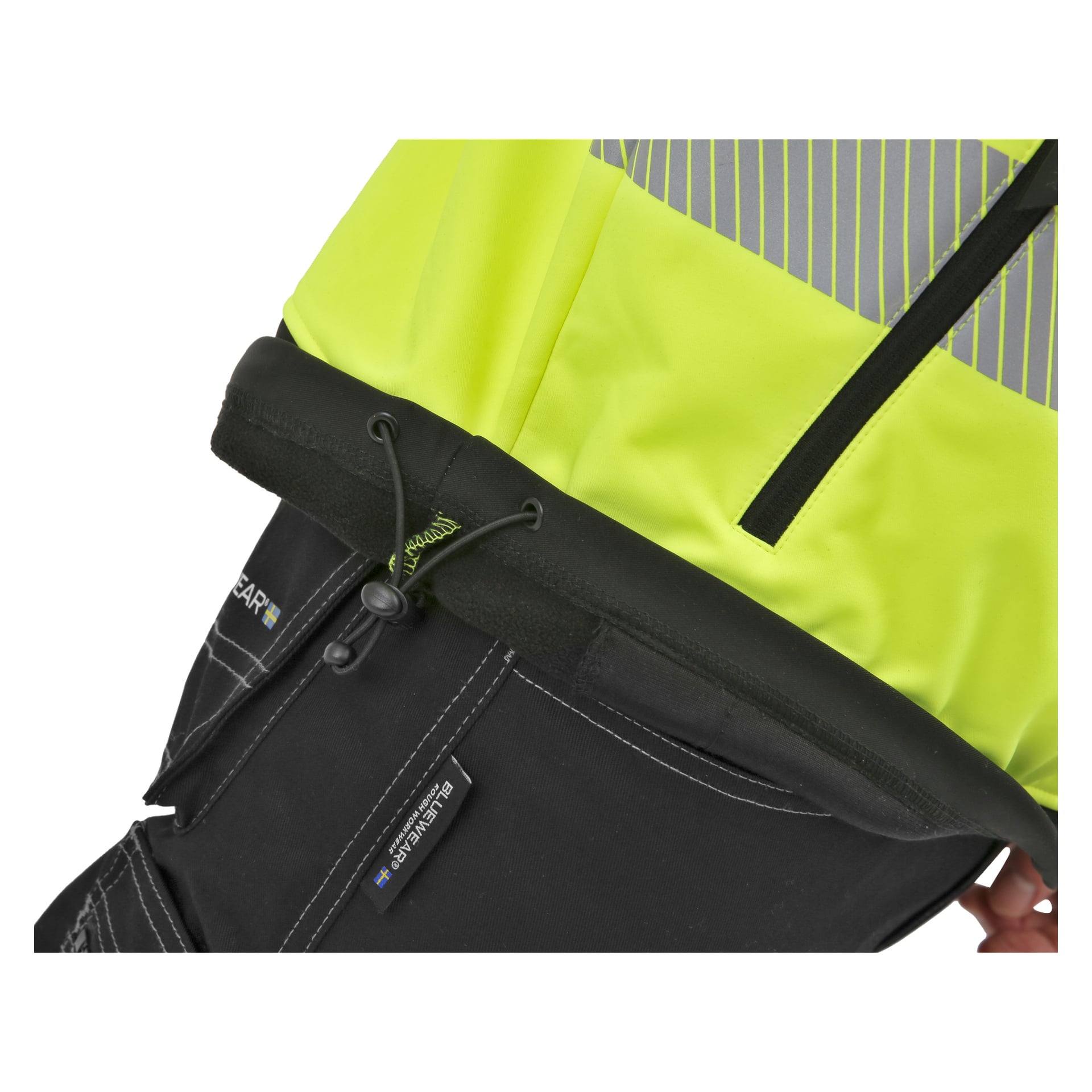 Närbild av Bluewear Hi-Vis Toronto softshelljacka i gult och svart, med reflekterande ränder, en ficka med dragkedja, justerbar manschettdragsko och framträdande sömmar längs det nedre svarta området.