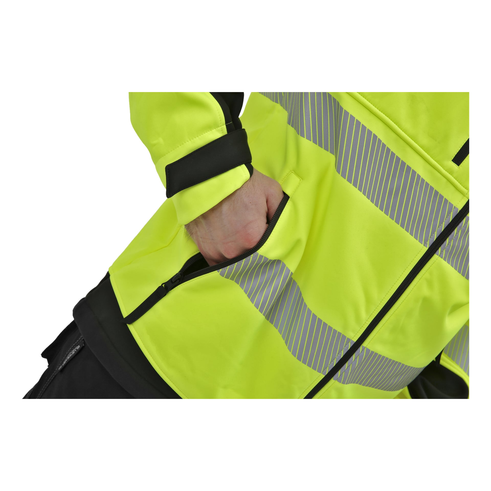 En person klädd i en ljusgul Bluewear Hi-Vis softshelljacka Toronto, med reflekterande ränder, skjuter in sin högra hand i en ficka med dragkedja. Bilden visar endast bålen och en del av en arm.