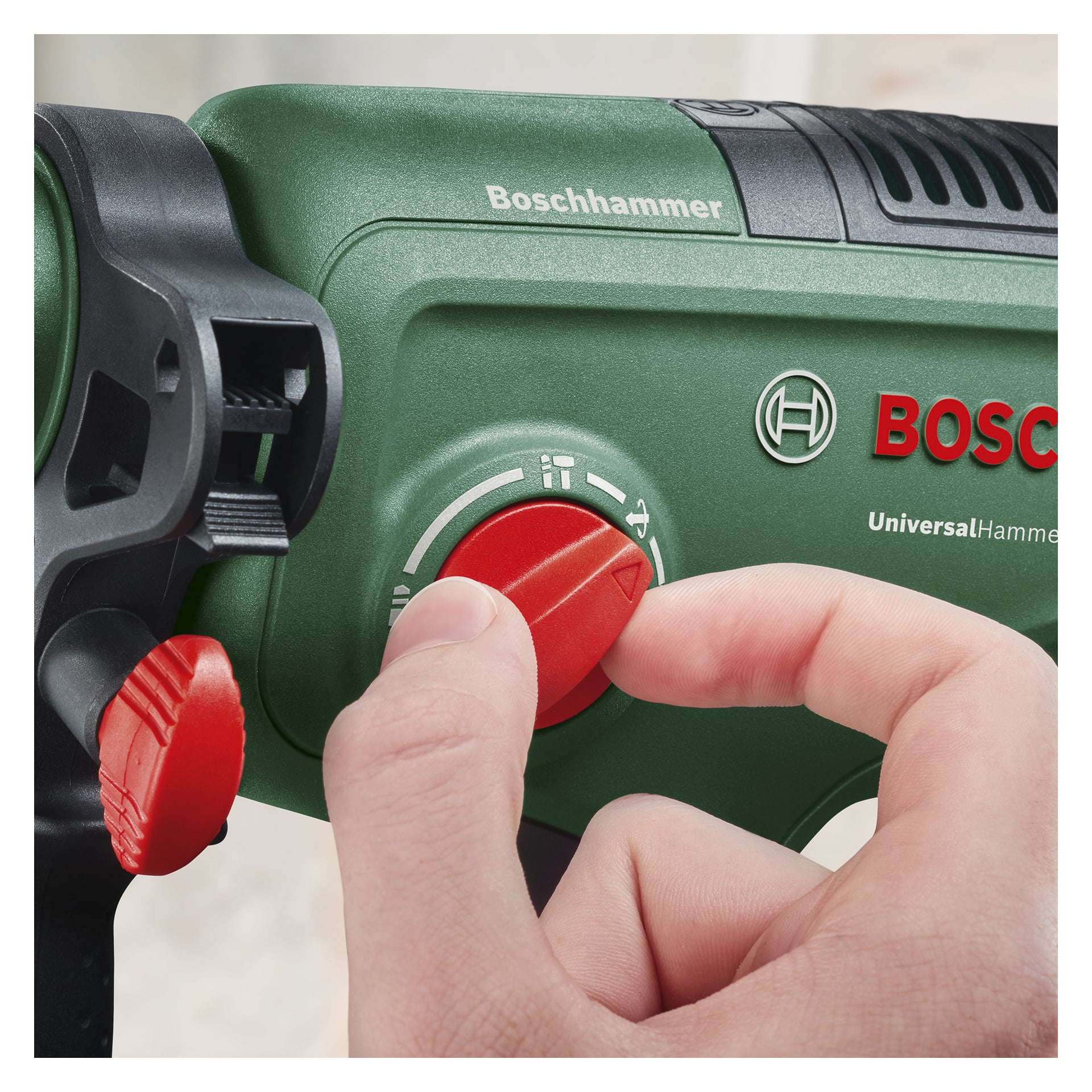 En hand justerar en röd ratt på en grön Bosch UniversalHammer 18V batteridriven borrmaskin. Verktyget har Bosch-logotypen och flera vita ikoner bredvid urtavlan.