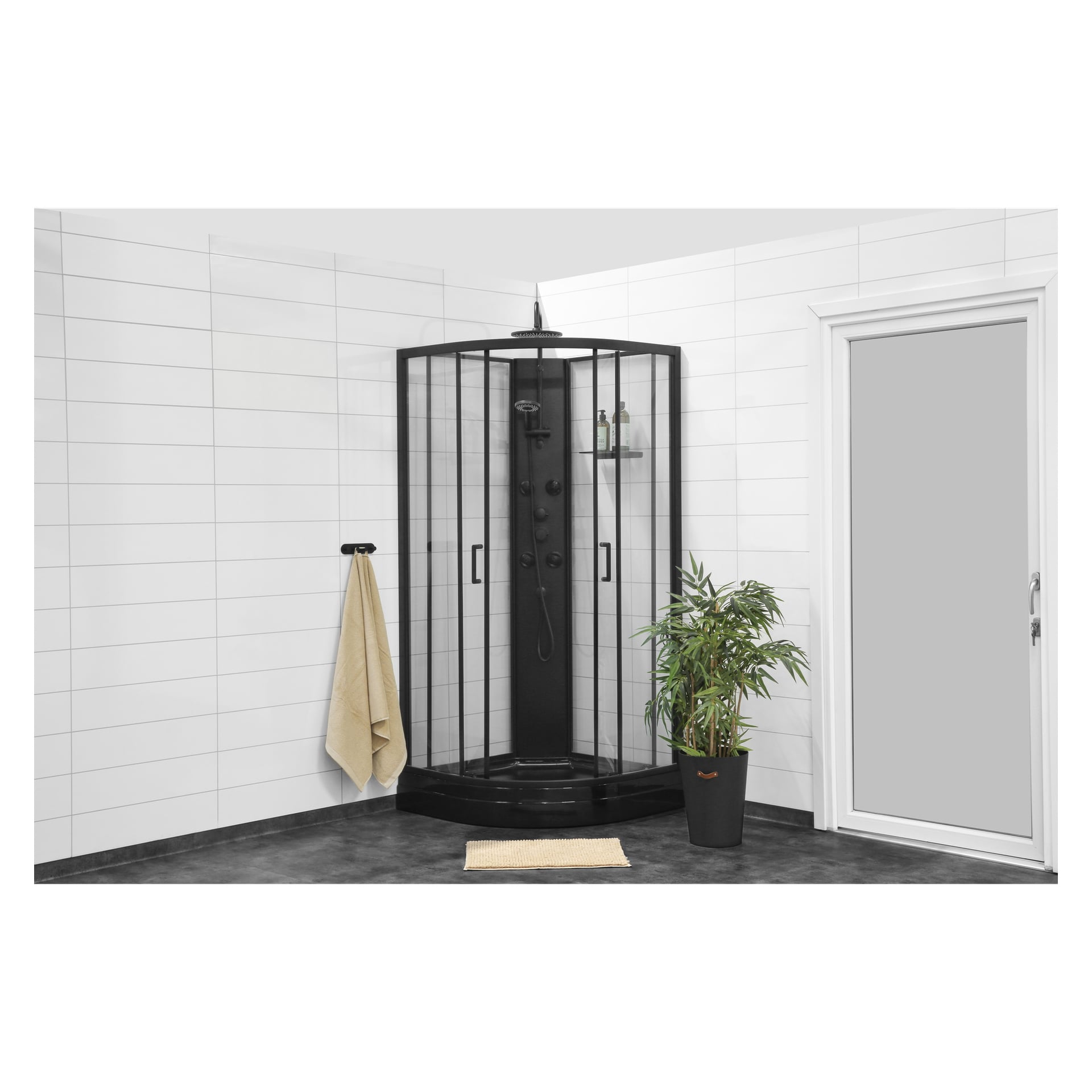 EKVIP sin svarte dusjkabin har en dusj over taket og elegante glassdører, plassert av hvite flislagte vegger. I nærheten henger et beige håndkle, og en liten beige matte ligger på det mørke gulvet. En grønn potteplante står ved siden av en frostet glassdør.