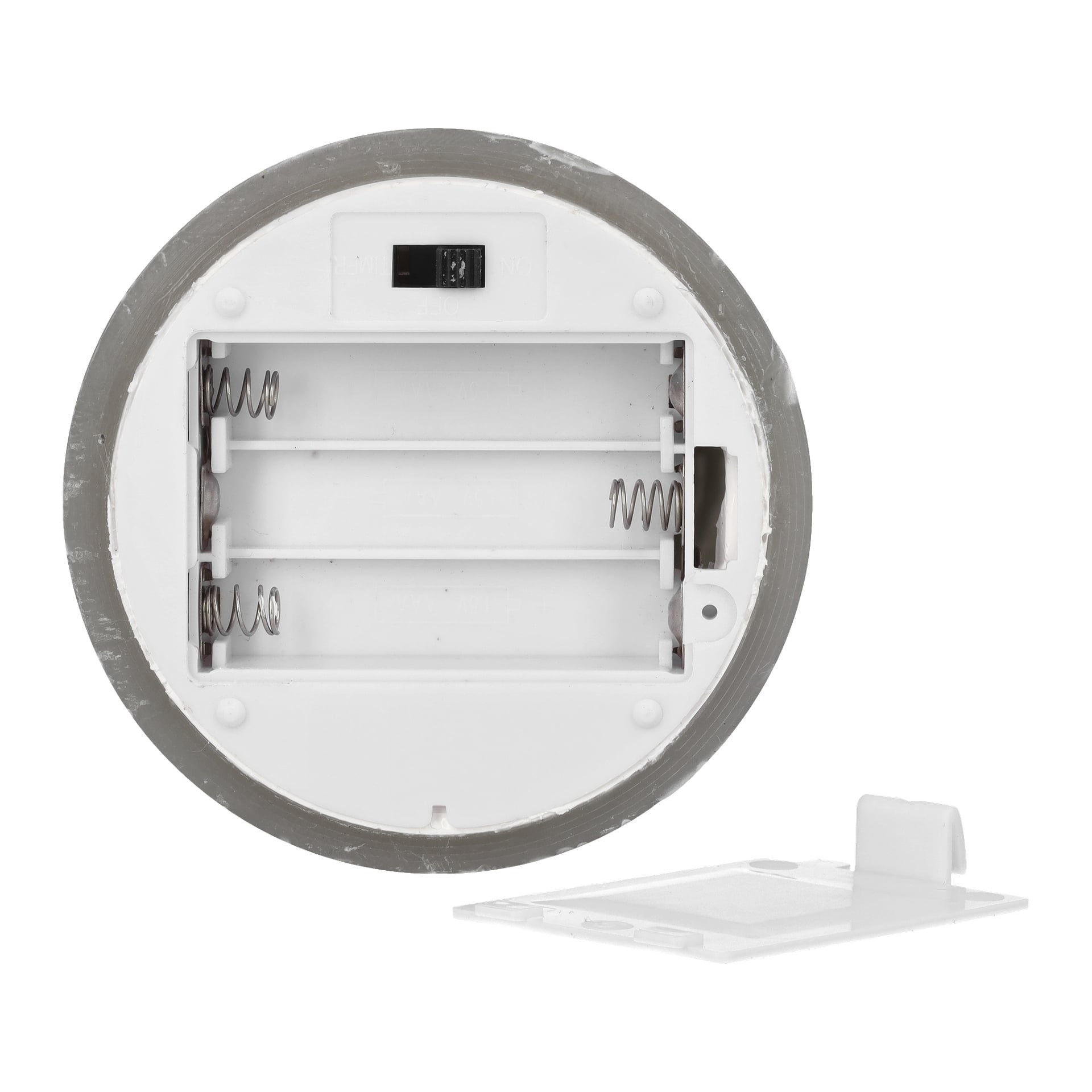 Ett runt, vitt plastbatterifack för Menuett Pillar Candle med en fladdrande LED-låga är öppet, dess avtagna lock ligger framför. Det finns tre platser för AA-batterier.