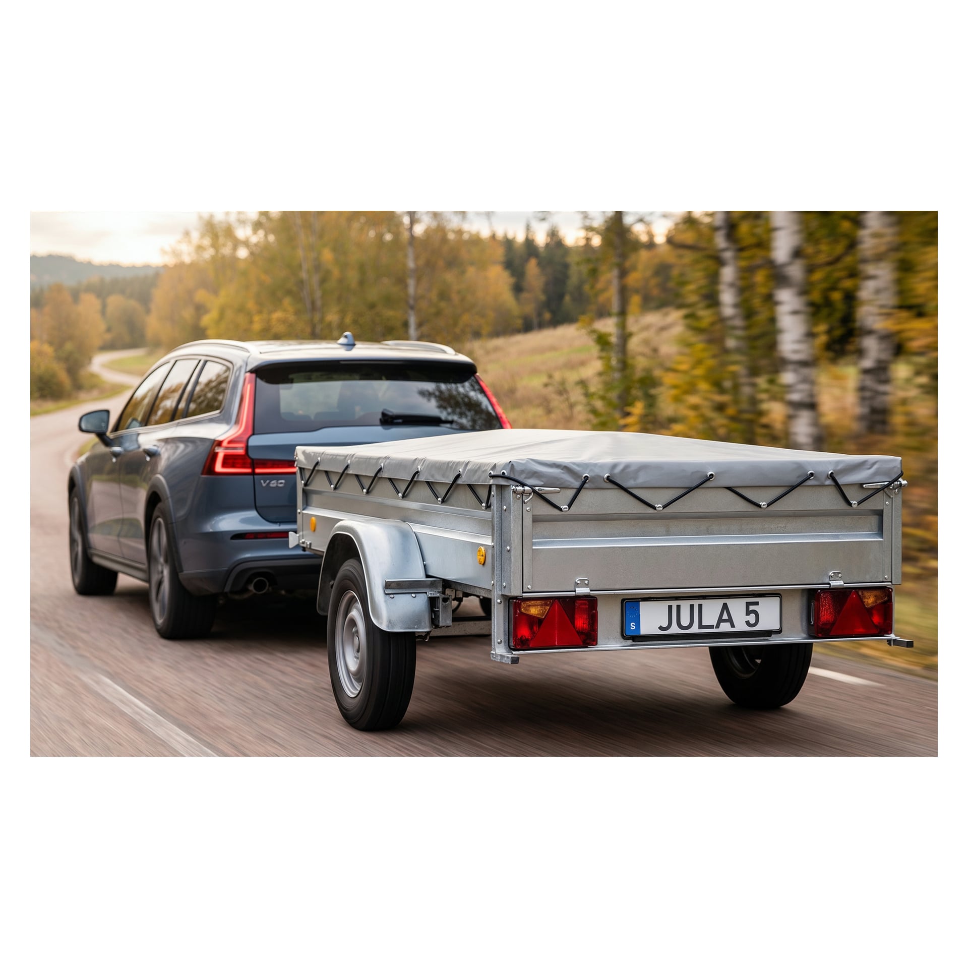 En mörk kombi drar en täckt släpvagn märkt "JULA 5" längs en stenlagd väg kantad av höstträd.