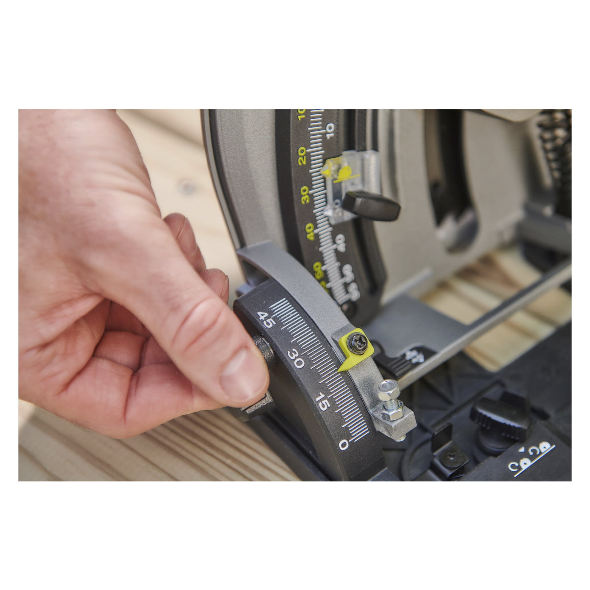 En hand flyttar vinkeljusteringen på Ryobi One+ HP batteridriven dyksåg med styrskena RPLS18X-0, vilket placerar indikatorn nära 45-gradersmarkeringen på gradskivans skala. Sågen placeras på en ljus träyta.