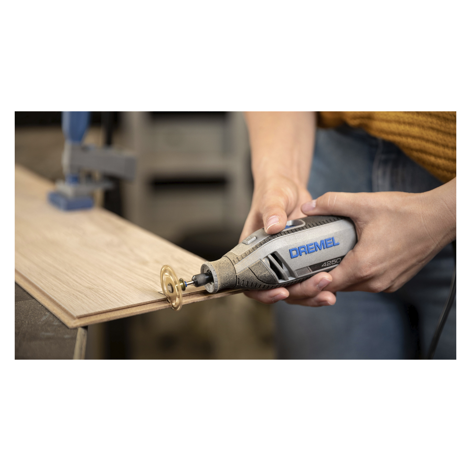 En person håller ett Dremel-roterande verktyg utrustat med en SC544 SpeedClic-skärskiva i båda händerna medan de skär en träbit, med en del av arbetsytan synlig i bakgrunden.