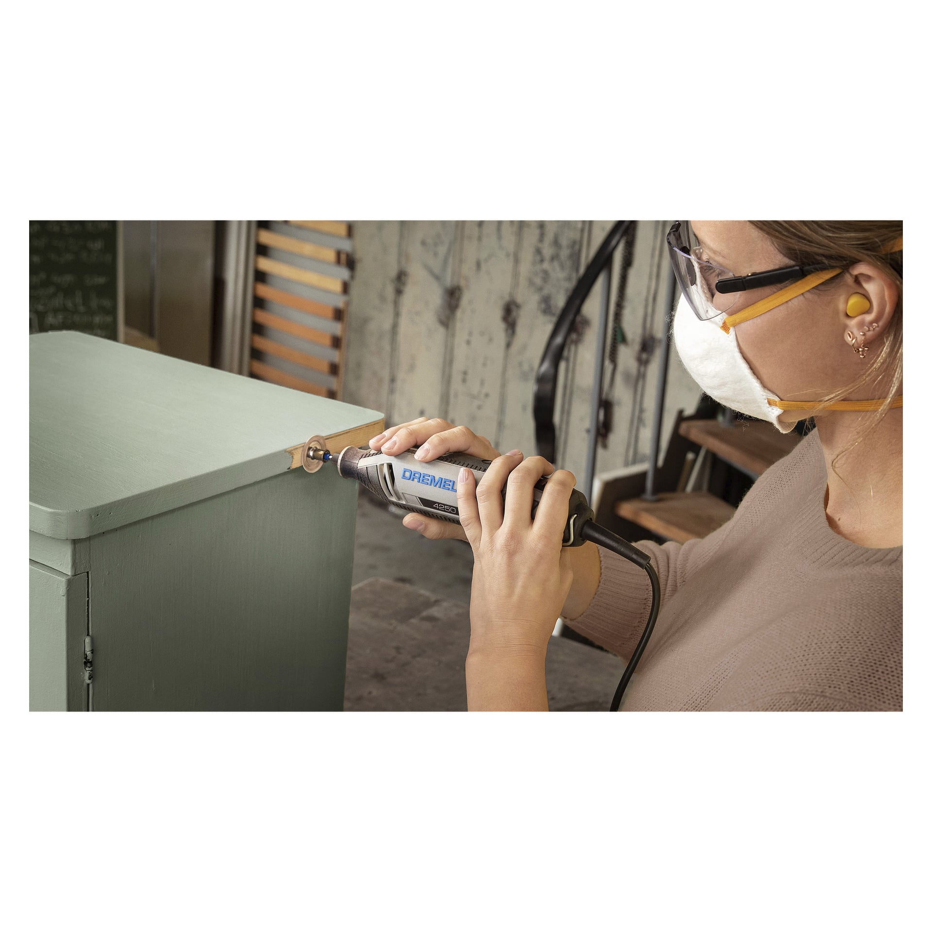 Någon utrustad med skyddsglasögon, mask och öronproppar använder Dremel SC411 SpeedClic slipskivor (paket om 6) för att slipa kanten på ett ljusgrönt träskåp.