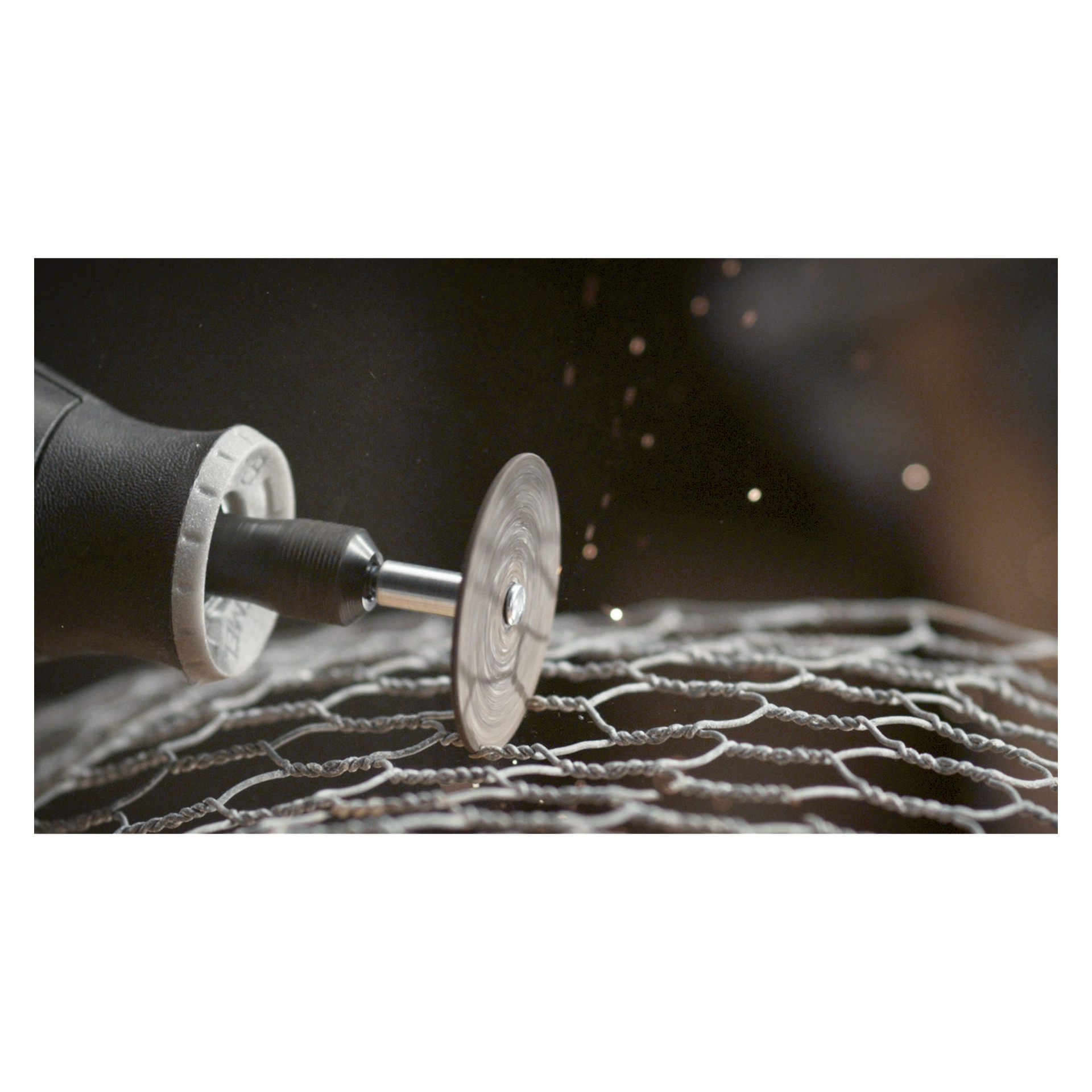 Et Dremel-skjærehjul 426 spinner mens det skjærer gjennom netting, og sprer metallgnister ved kontaktpunktet. Verktøyet og meshen er tydelig synlige i forgrunnen, mens bakgrunnen er ute av fokus.