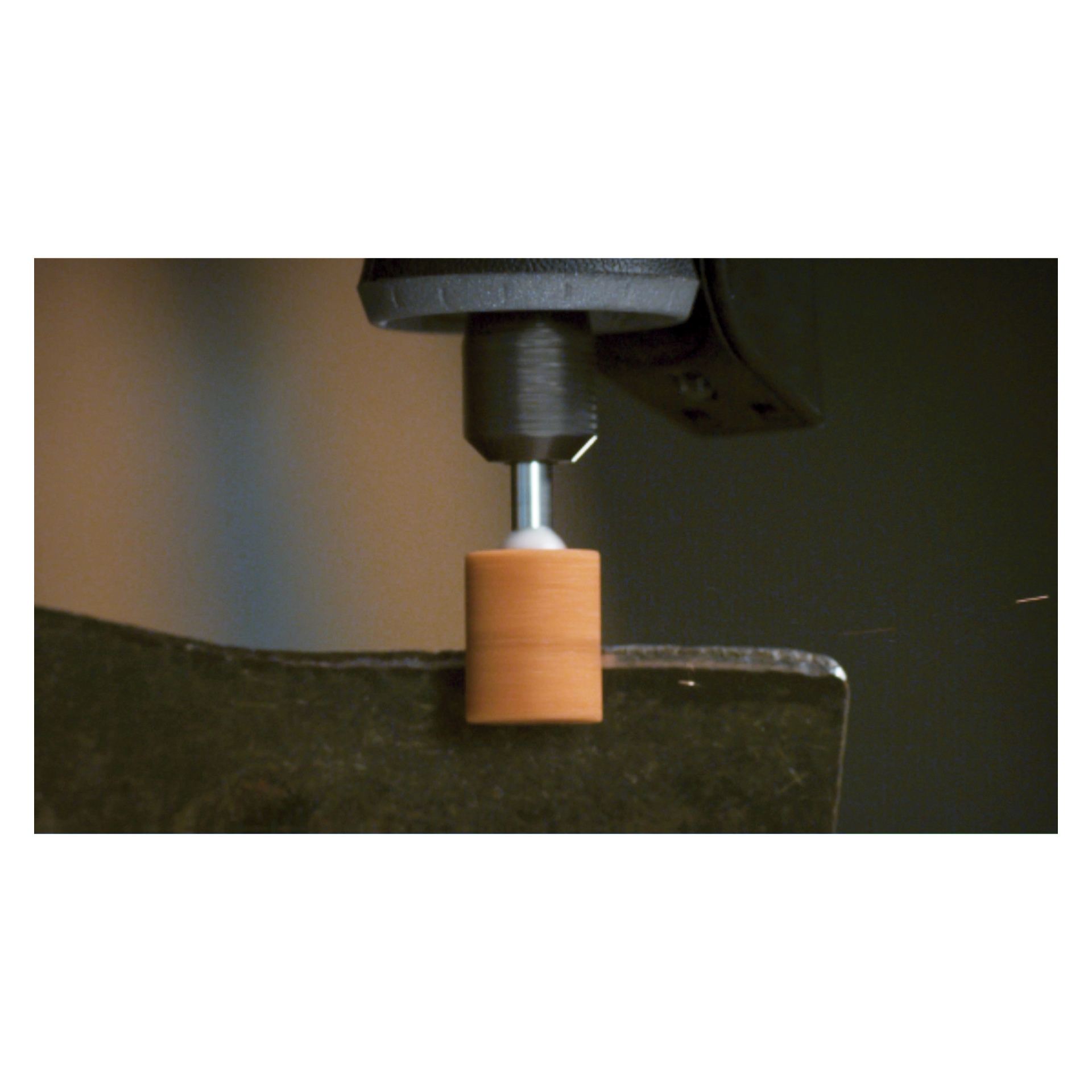 En detaljerad vy av ett Dremel-roterande verktyg utrustat med en Slipsten 932-fäste från ett set om tre, som noggrant slätar ut kanten på en platt, mörk metallyta.