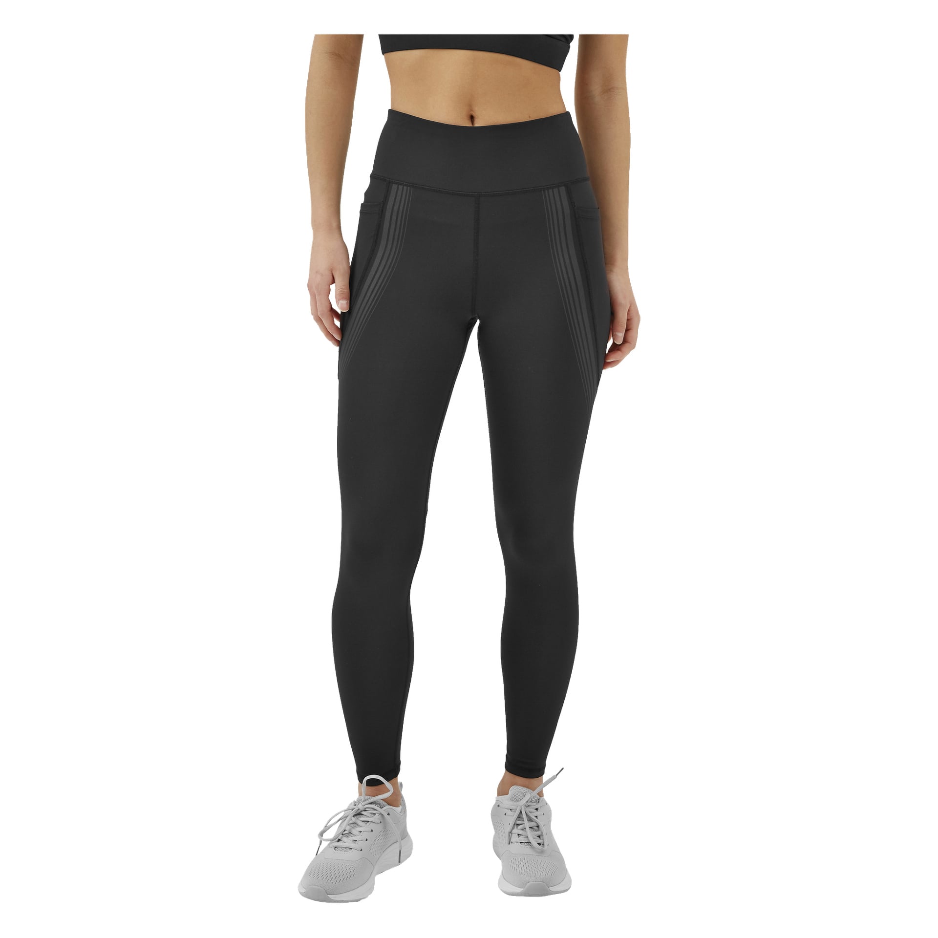 En person syns från midjan och neråt, klädd i svarta högmidjade Kayoba's Tights damleggings från Boston, en matchande svart sport-bh och grå sportskor, stående med armarna naturligt vilande vid sidorna.