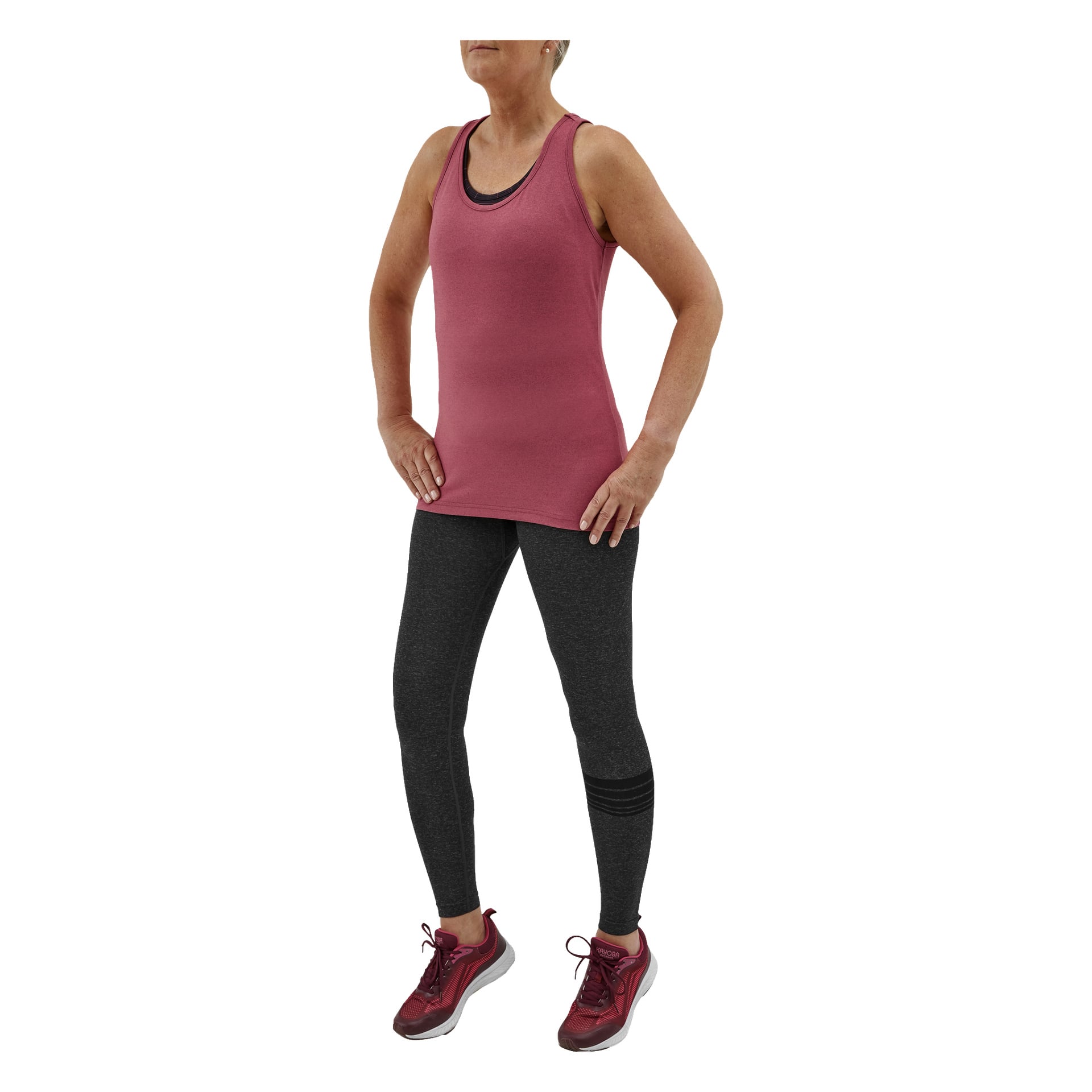 En person poserar med händerna på höfterna, klädd i mörkgrå Kayoba Seamless träningstights från San Diego, en rosa ärmlös topp och vinröda sneakers. Deras huvud är delvis synligt, vilket framhäver den atletiska outfiten.