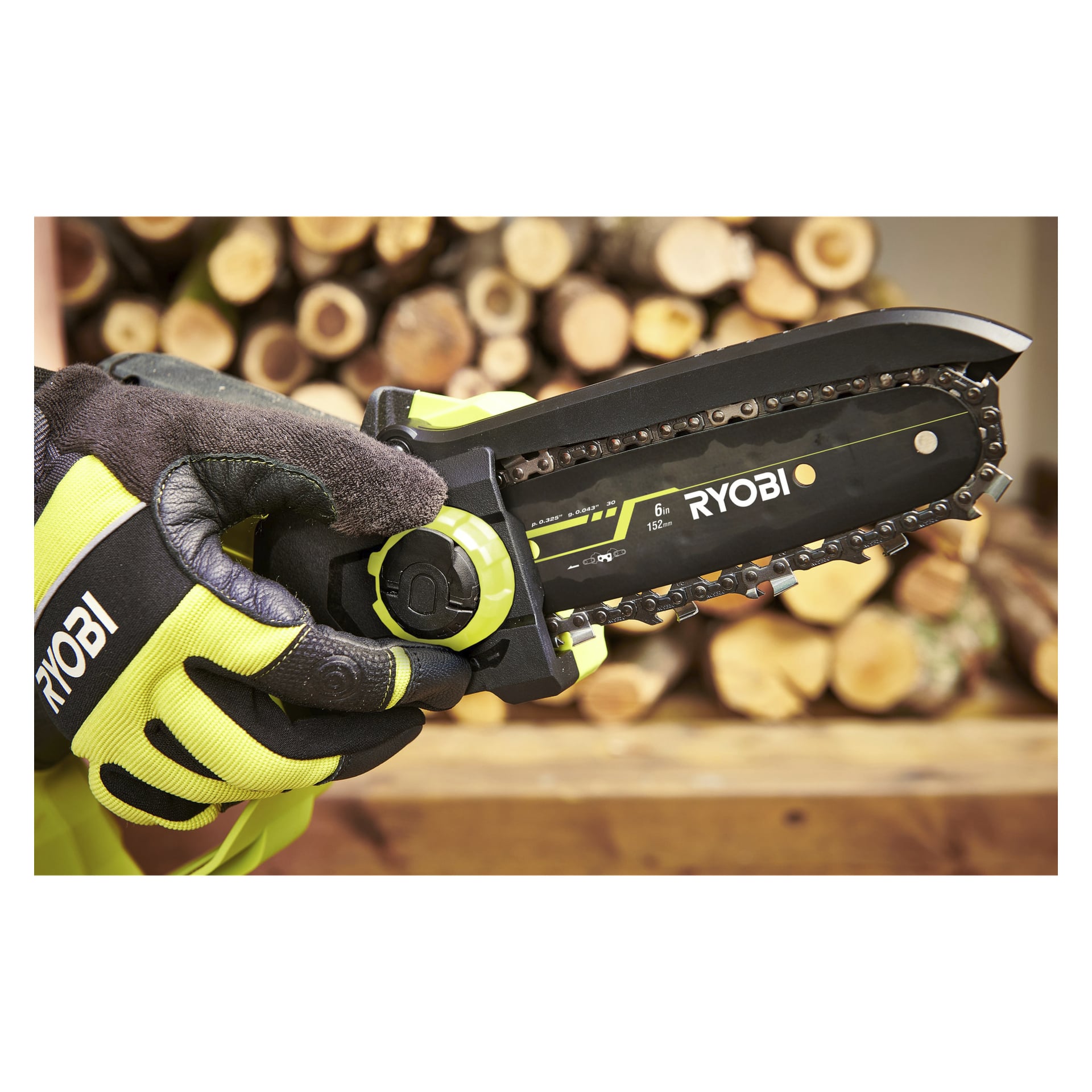 En handskbeklädd hand håller en Ryobi One+ HP batteridriven beskärningssåg RY18PSX15A-0, hållen framför en hög med sågade vedstockar. Bladet och den framträdande logotypen på sågen syns tydligt i förgrunden.