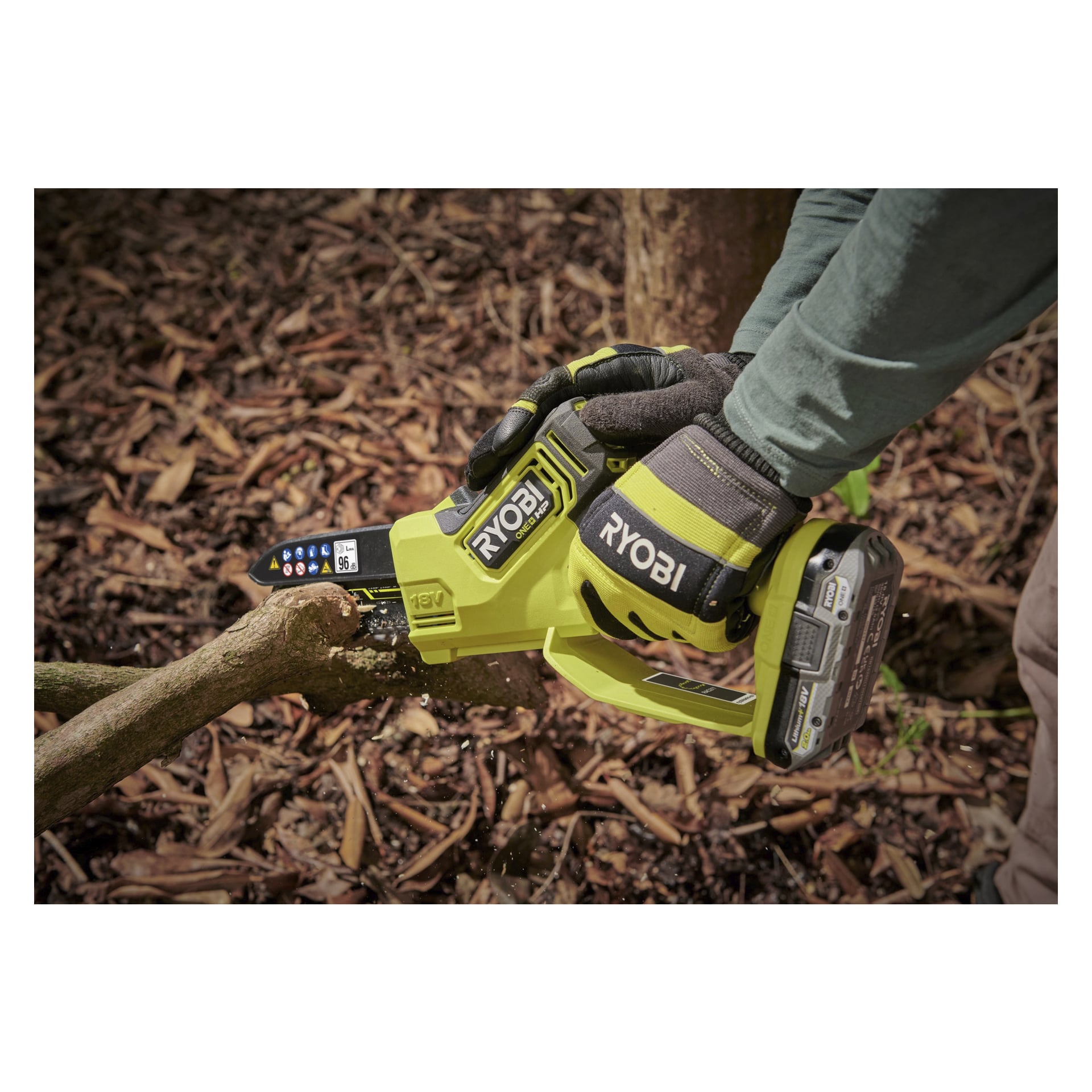 En person som bär handskar använder en Ryobi One+ HP batteridriven beskärningssåg RY18PSX15A-0 för att trimma en trädgren utomhus, med torra blad synliga på marken nedanför.