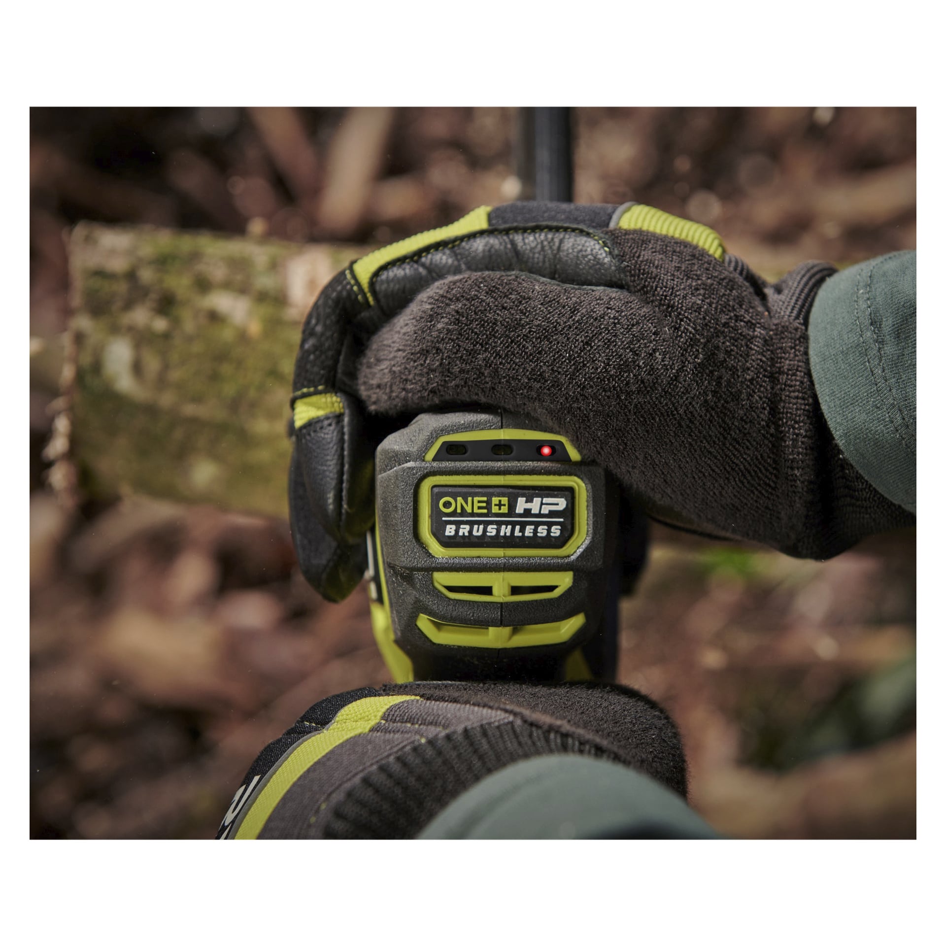 Någon med mörka handskar håller Ryobi One+ HP batteridrivna beskärningssåg RY18PSX15A-0 utanför, vilket framhäver sågens handtag och synliga märkning, med ett litet rött LED-ljus som lyser.
