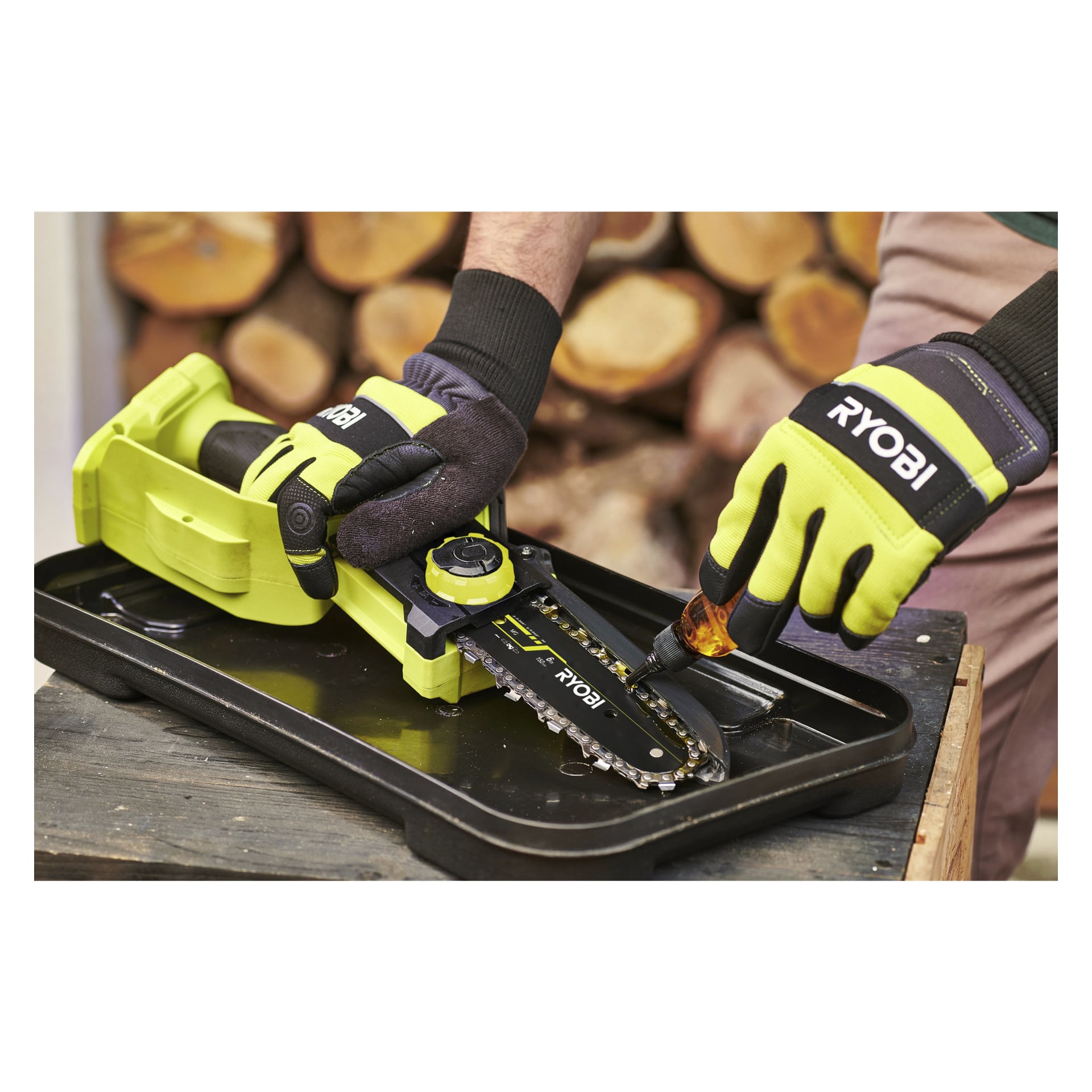 Med Ryobi-handskar på använder någon en skruvmejsel för att dra åt kedjan på en Ryobi One+ HP batteridriven beskärningssåg (modell RY18PSX15A-0), som står på en bricka med vedstaplar bakom.