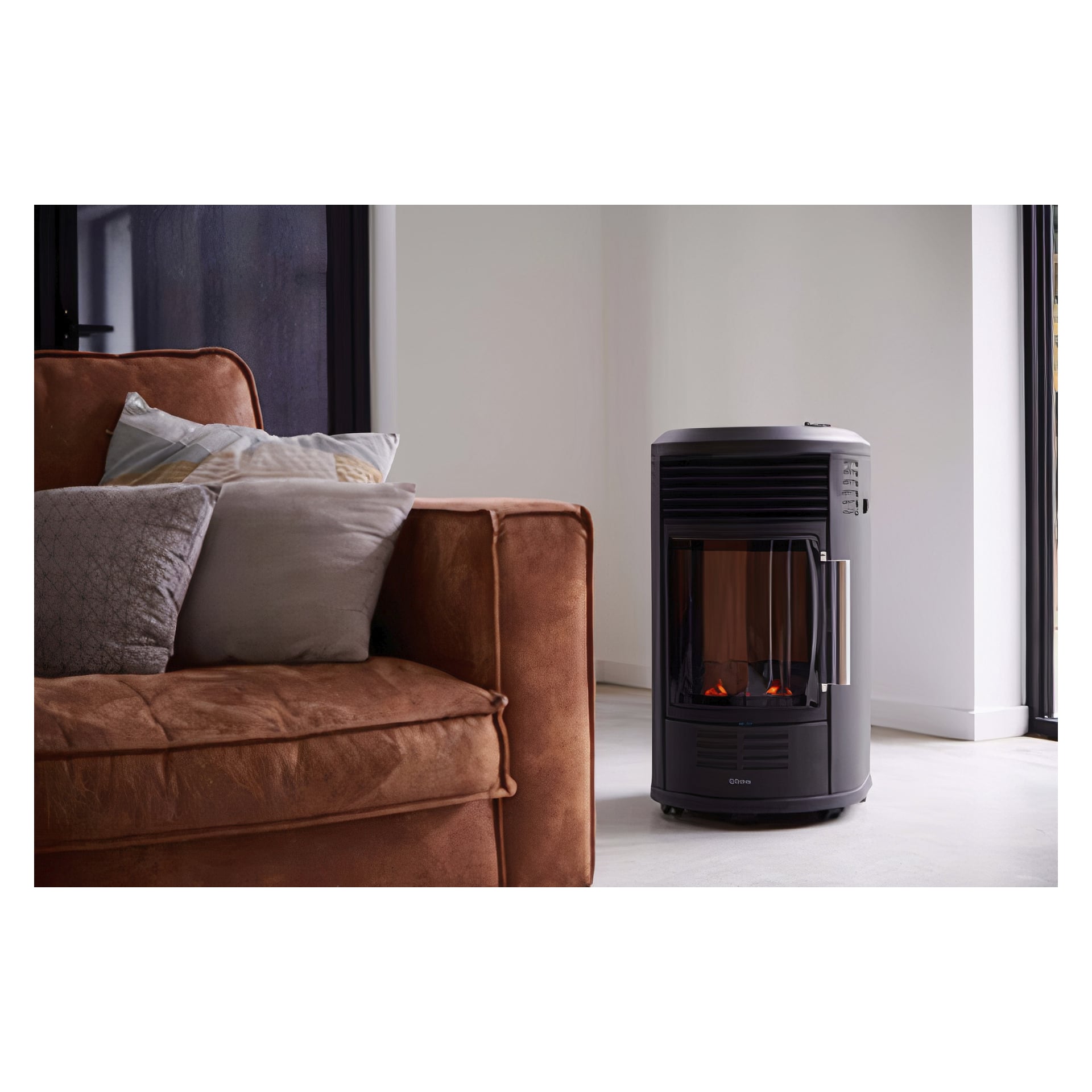 En brun sofa med flere puter står ved siden av en Qlima LPG-ovn GH8034, med glassfront som viser en simulert flamme, alt plassert på et lyst gulv i et moderne rom.
