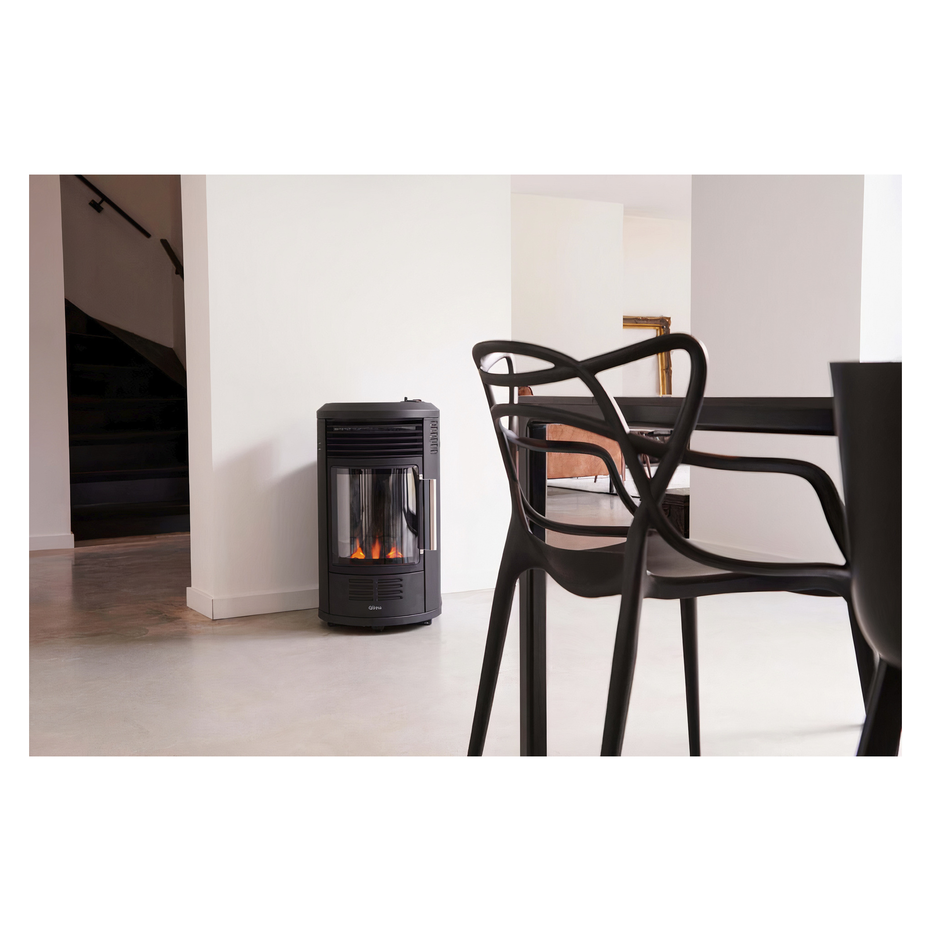 En slank svart Qlima GH8034 LPG-ovn med synlig flamme er plassert i et minimalistisk rom; Svarte designerstoler og et spisebord står på et polert gulv i forgrunnen.