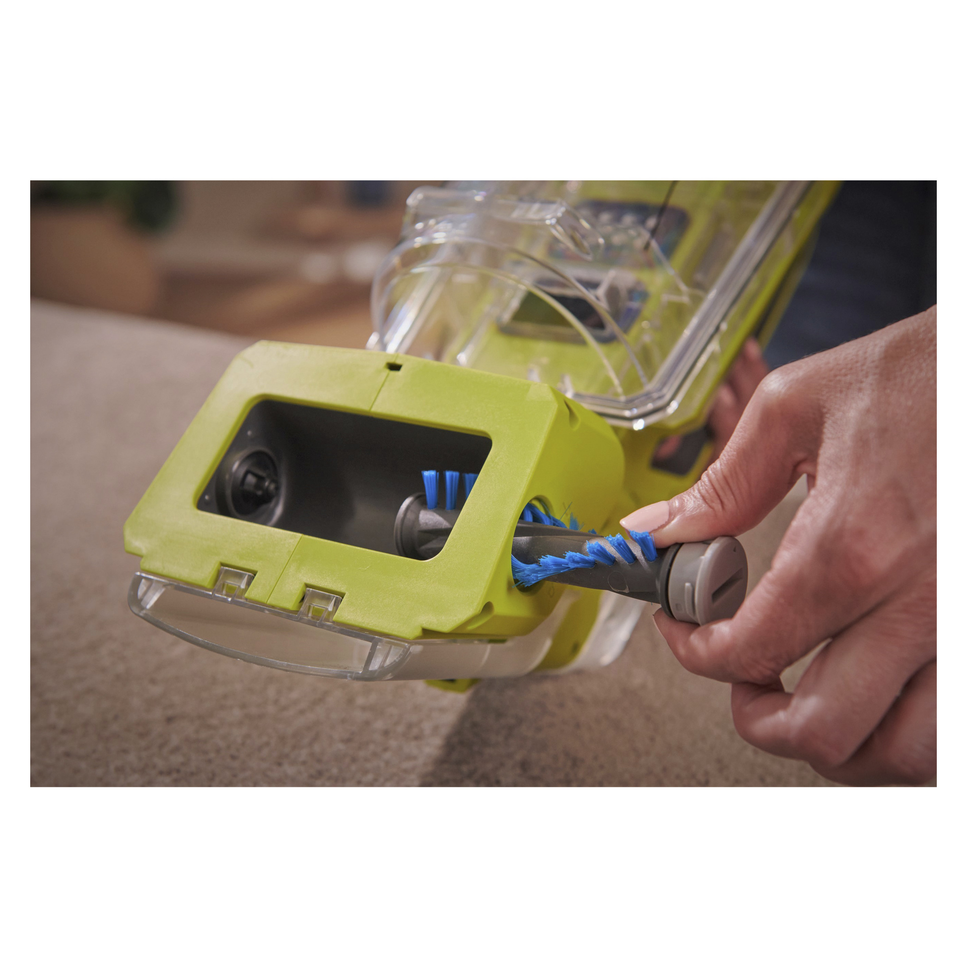 Ktoś wkłada wałek do szczotki z niebieskim włosiem do zielonego Ryobi One+ Swift Clean RDC18-0 do usuwania plam zasilanego baterią, przygotowując go do czyszczenia dywanu.
