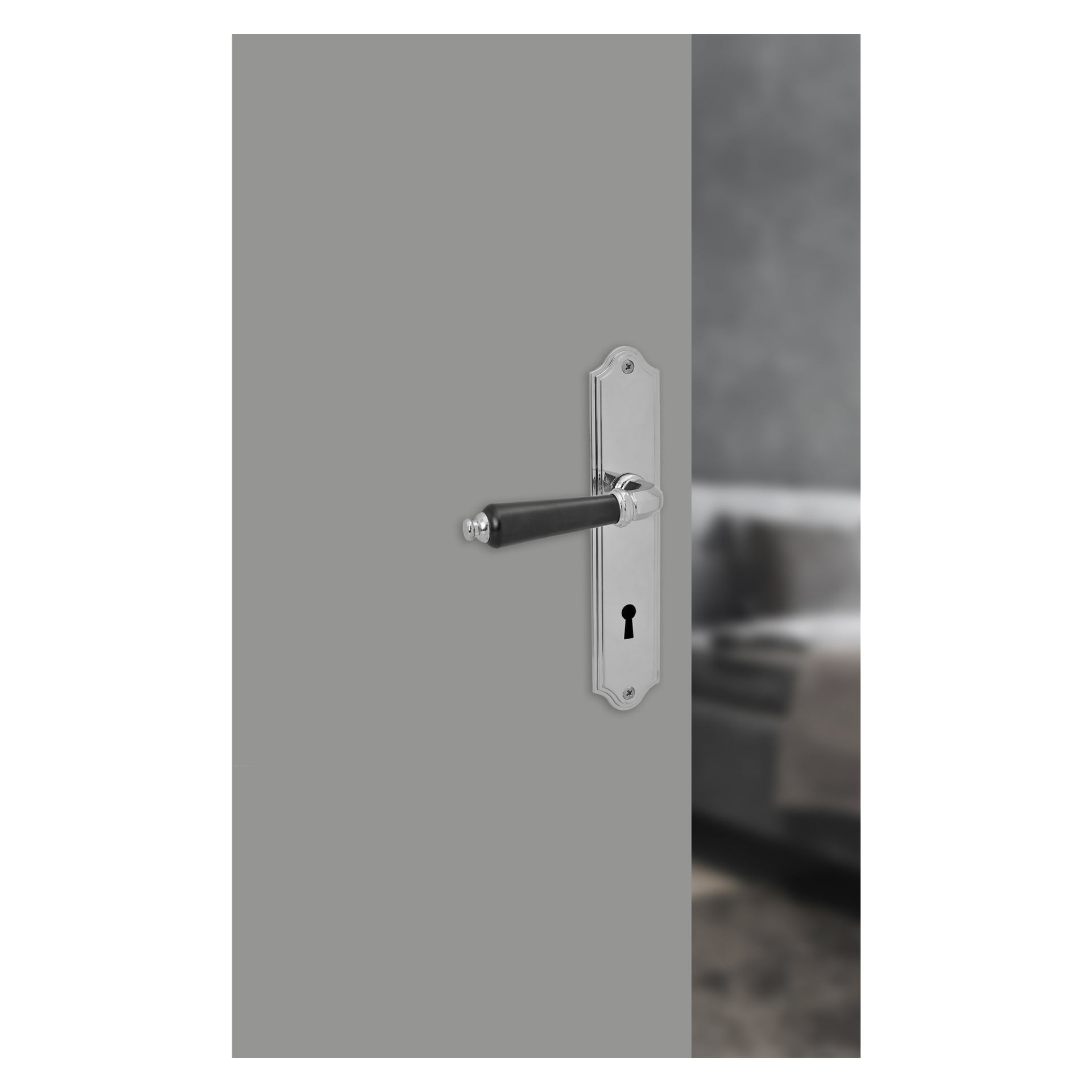 Eine Nahaufnahme des Hard Head Innentürgriffs C Chrome zeigt seine glänzende silberne Oberfläche mit schwarzem Griff und Schlüsselloch, das in eine graue Tür eingelassen ist, mit einem sanft verschwommenen Raum und Sofa im fernen Hintergrund.
