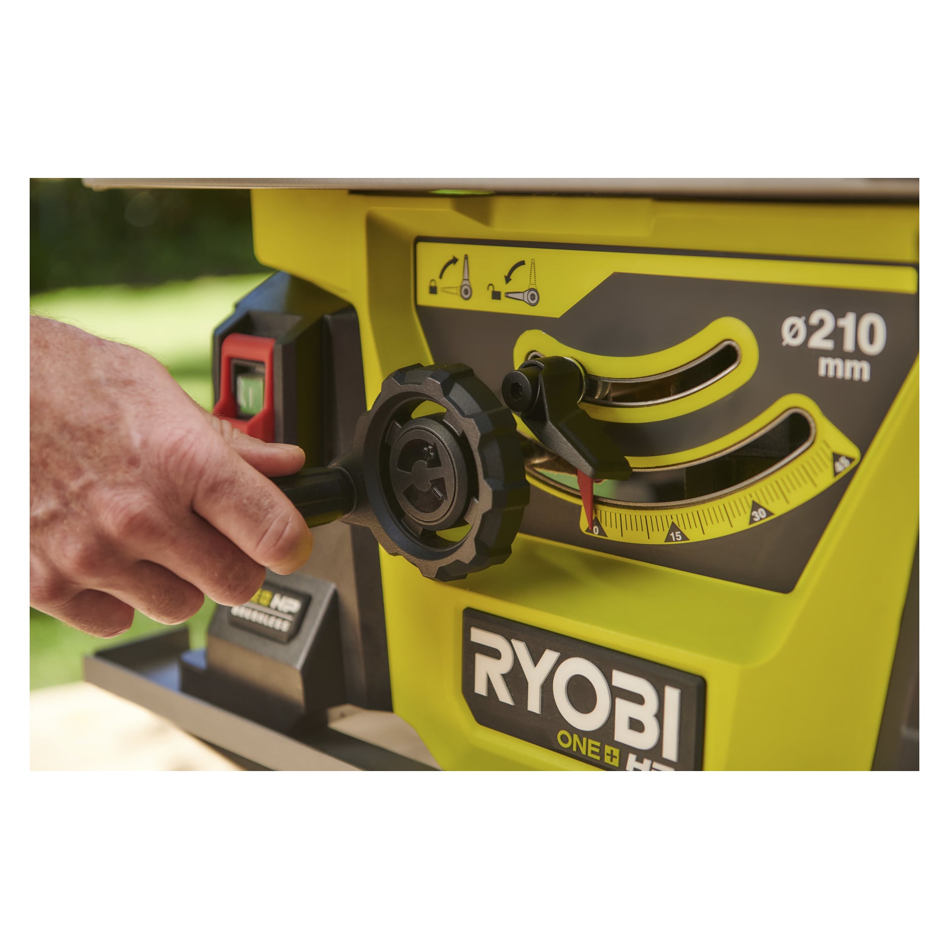 En hand vrider på den svarta ratten på en gul Ryobi One+ HP RTBS18X-0 batteridriven bordsåg, som visar mätrattar och märkta instruktioner på maskinen. Bilden framhäver både den justerande handen och mekanismen.