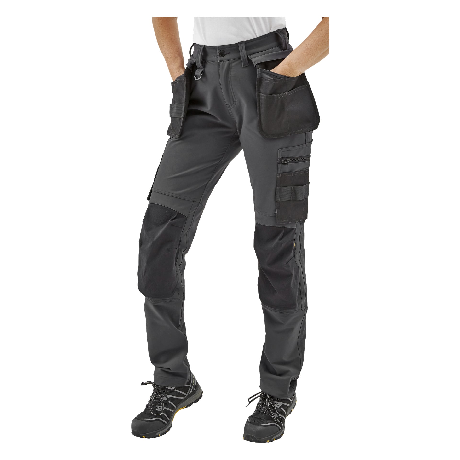 En person i Bluewear Pro Workwear Women's work pants Stella med flera fickor och förstärkta knän, svarta arbetsskor, endast underkroppen synlig och händerna instoppade i fickorna.