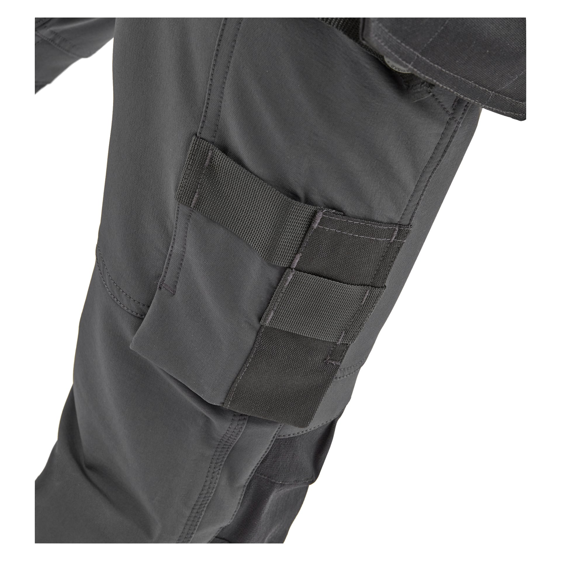 Närbild som visar någon klädd i mörkgrå Stella damarbetsbyxor från Bluewear Pro Workwear, med en lårficka accentuerad av svarta axelband; en del av jackans övre ben och fåll kan också ses.