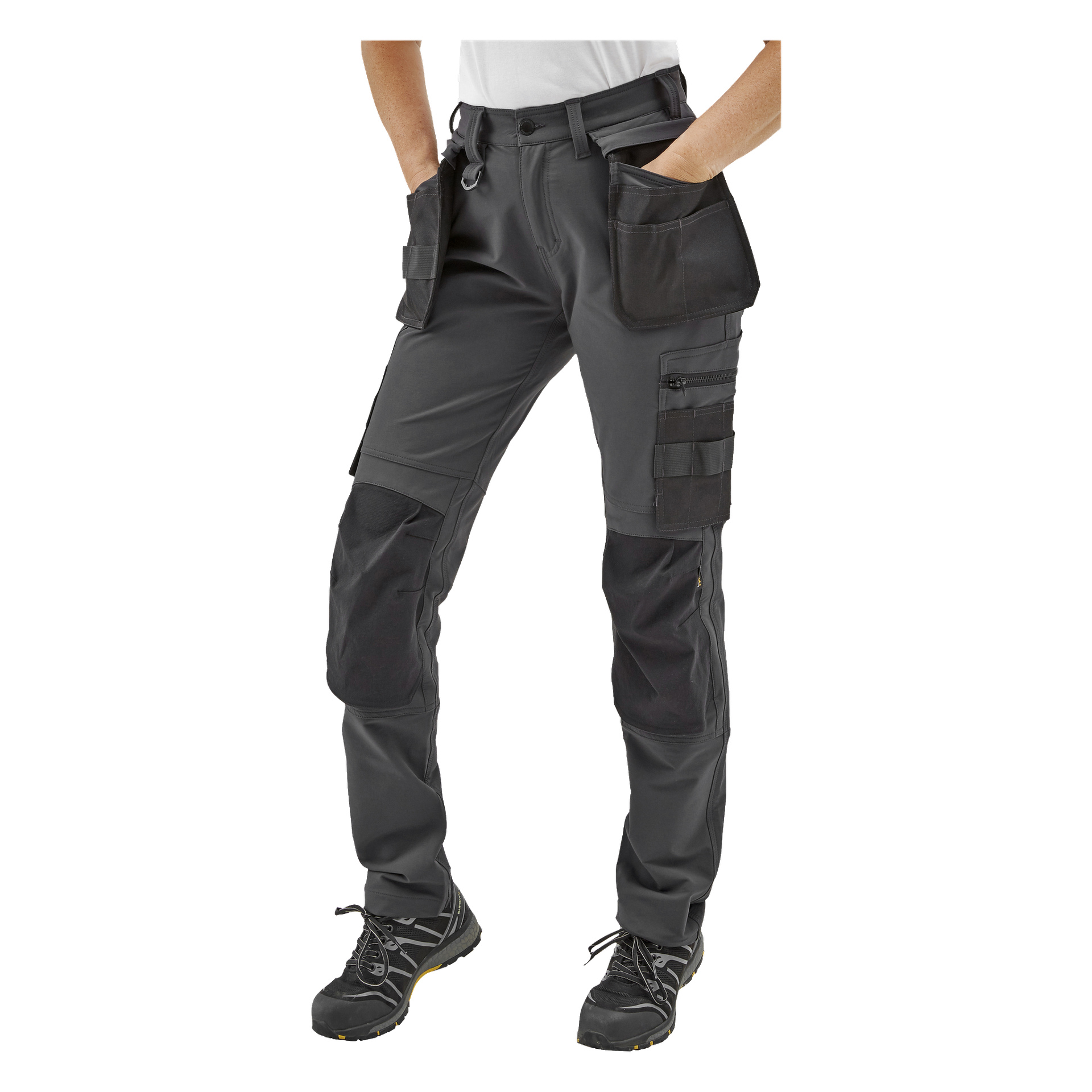Person i Bluewear Pro Workwear Stella damarbetsbyxor med förstärkta knän, verktygsöglor, dragkedjedelar, flera fickor och svarta skor med gula detaljer; händerna instoppade i framfickorna.