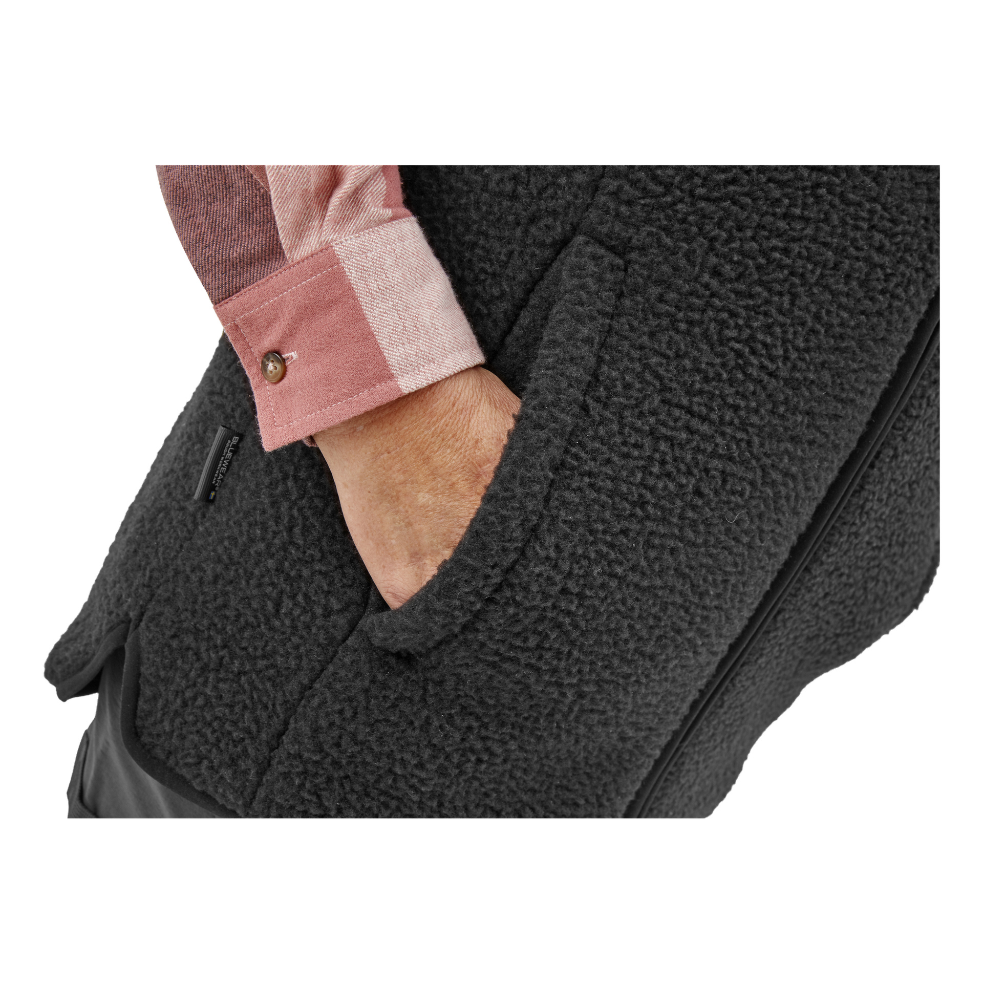 Någon i en rosa rutig skjorta modellerar Bluewear Women's pile vest Vivi, deras hand nedstoppad i en sidoficka som visar plaggets texturerade tyg och synliga sömmar.