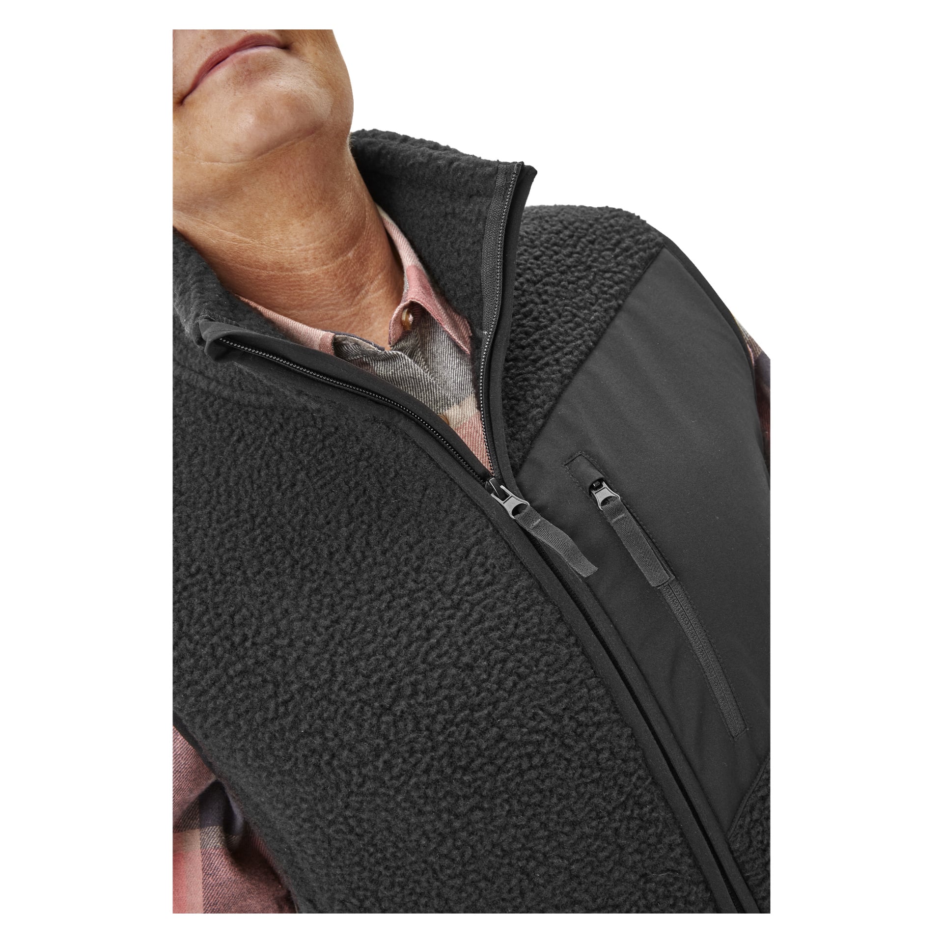 En person, synlig från hakan och neråt, är klädd i en rosa rutig skjorta med Bluewear Women's pile vest Vivi—en svart fleeceväst med dragkedja och bröstficka.