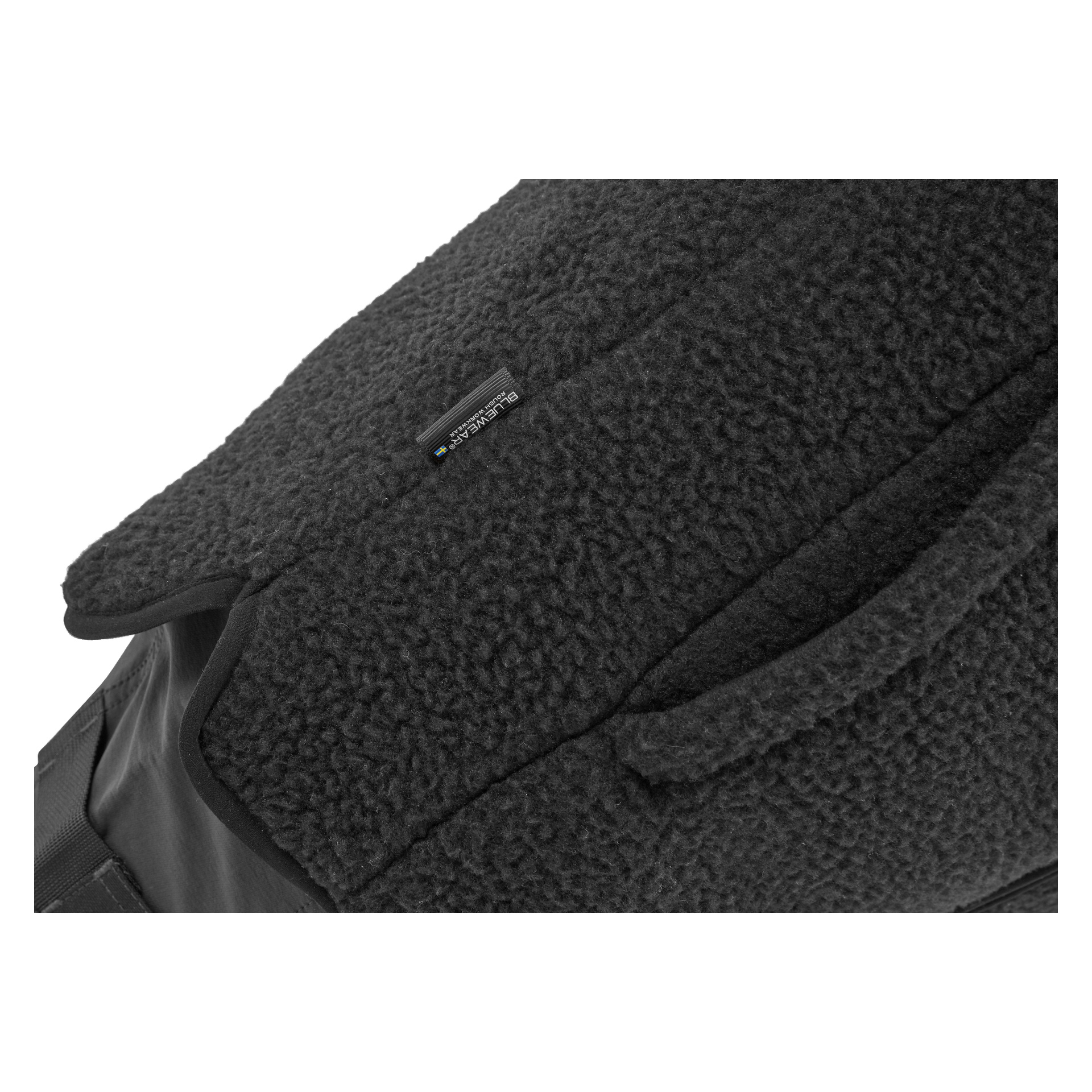 En närbild av damvästen Vivi från Bluewear framhäver dess svarta fleece- eller sherpa-liknande textur, med en liten rektangulär etikett där det står "bluesign product." Fokus ligger på den mjuka ytan och precisa skarvdetaljer.